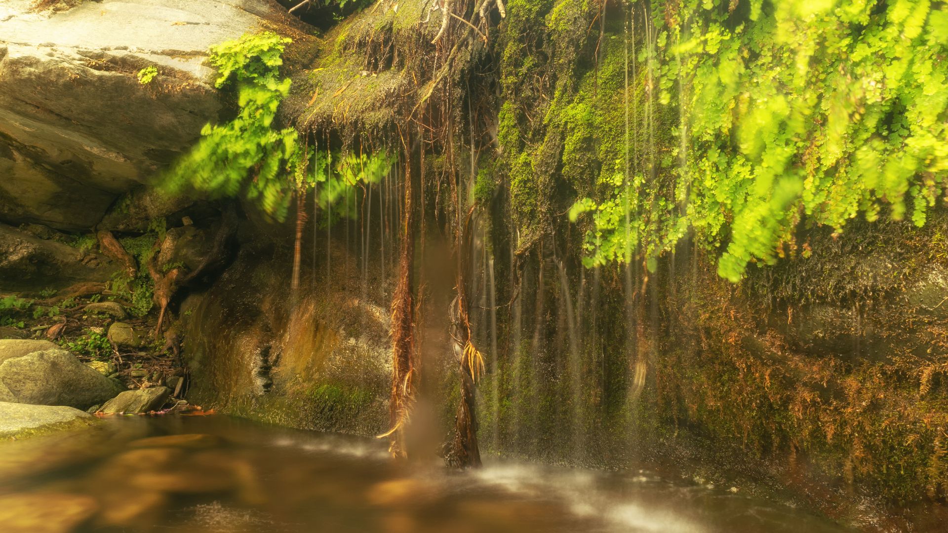 Pithara Waterfall in Andros, Greece, with water cascading over rocks and through lush vegetation.