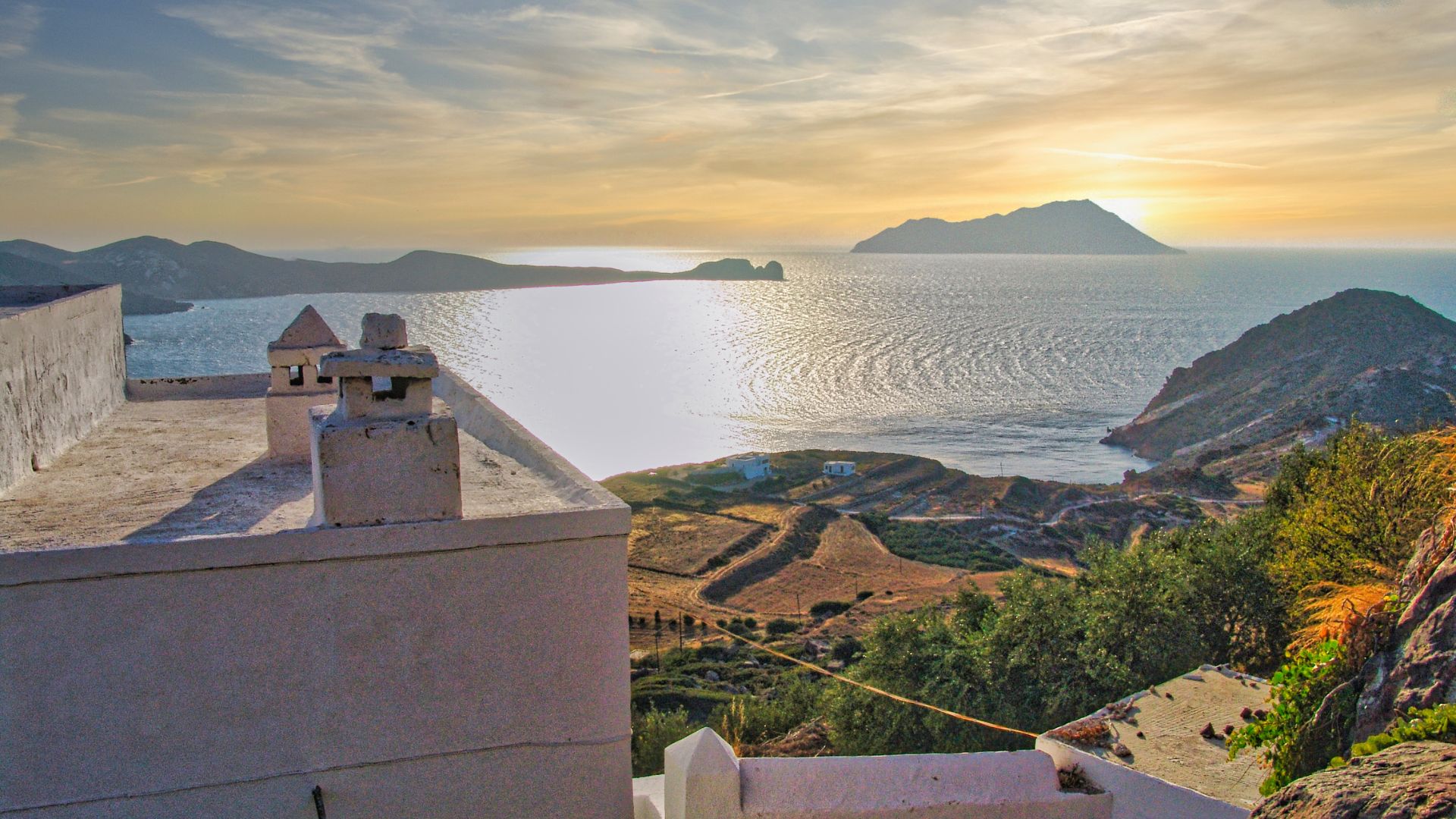 Scenic view of Plaka village in Milos, Greece, with white buildings, the Aegean Sea, and a distant island.