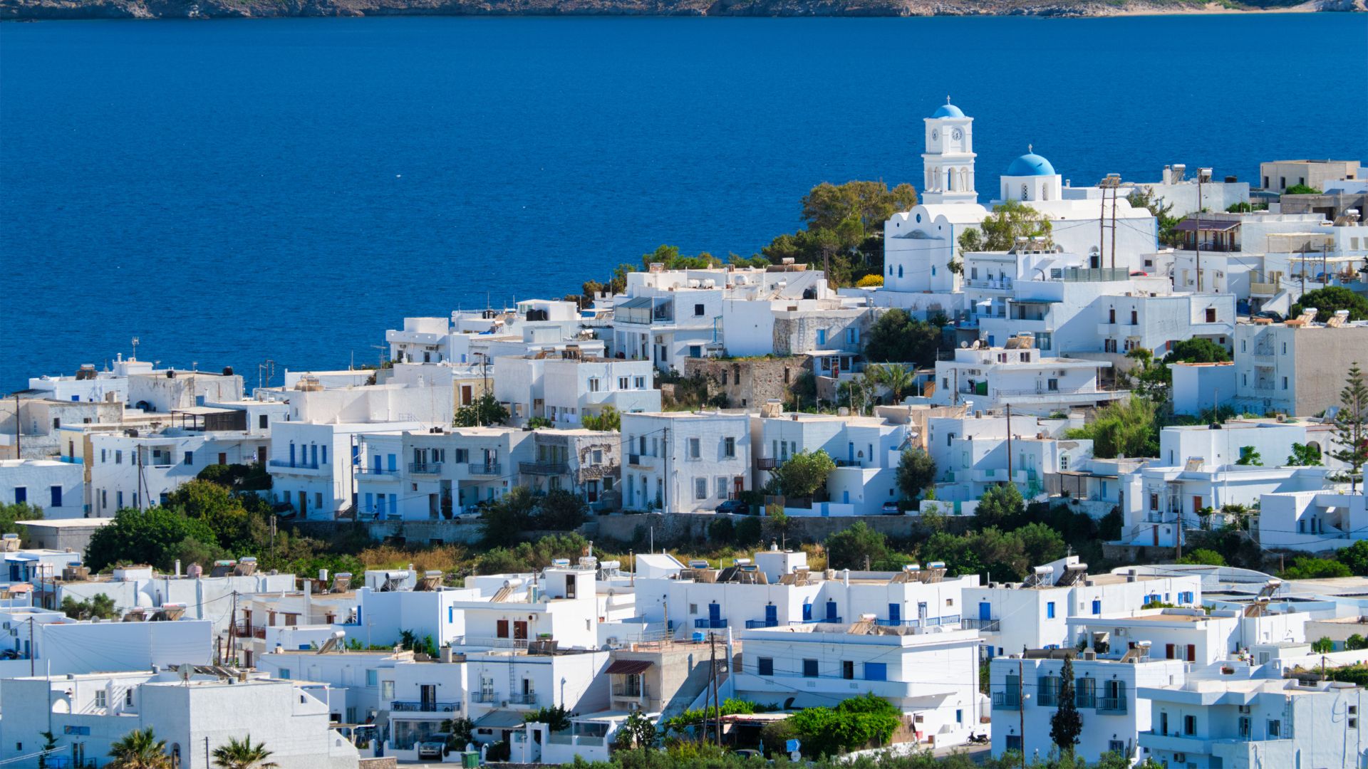 A scenic view of Plaka village in Milos, Greece, featuring white houses and a blue sea backdrop.