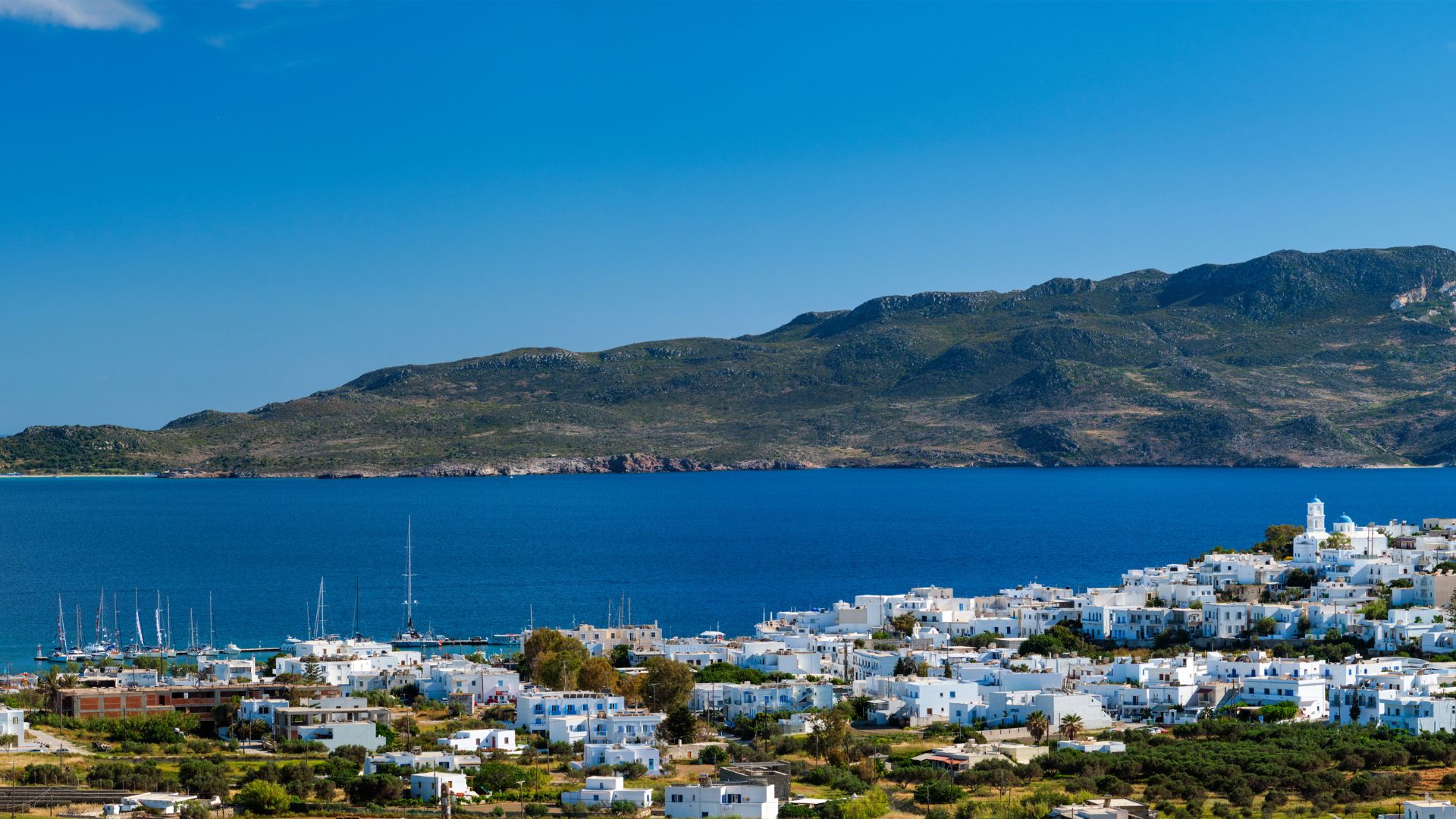 A scenic view of Plaka village in Milos, Greece, featuring white houses and a blue sea backdrop.