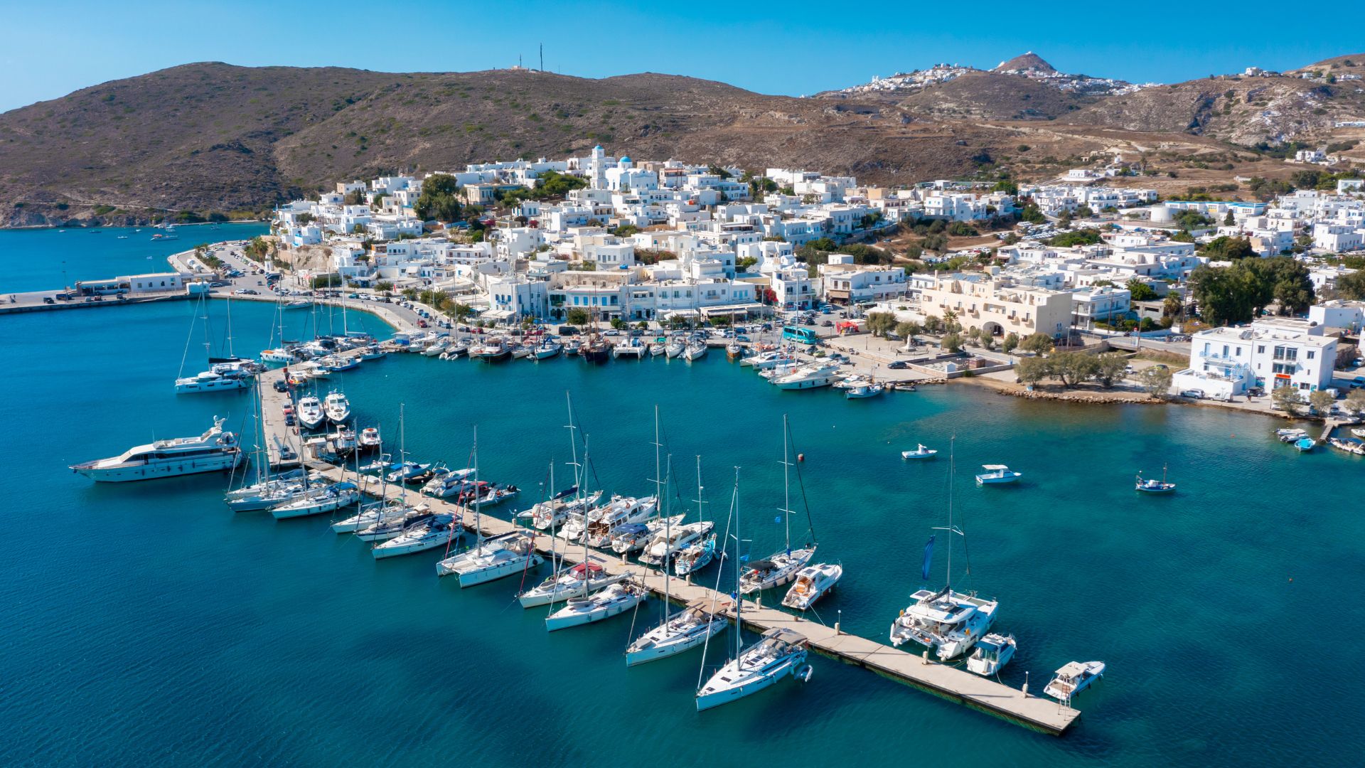 Aerial view of Adamantas harbor, Milos, Greece, showcasing a scenic port with white buildings and numerous boats docked.
