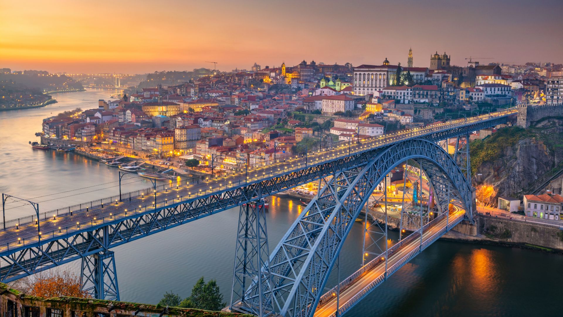 Dom Luís I Bridge spanning the Douro River in Porto, Portugal, connecting Porto and Vila Nova de Gaia with boats docked along the riverbank.