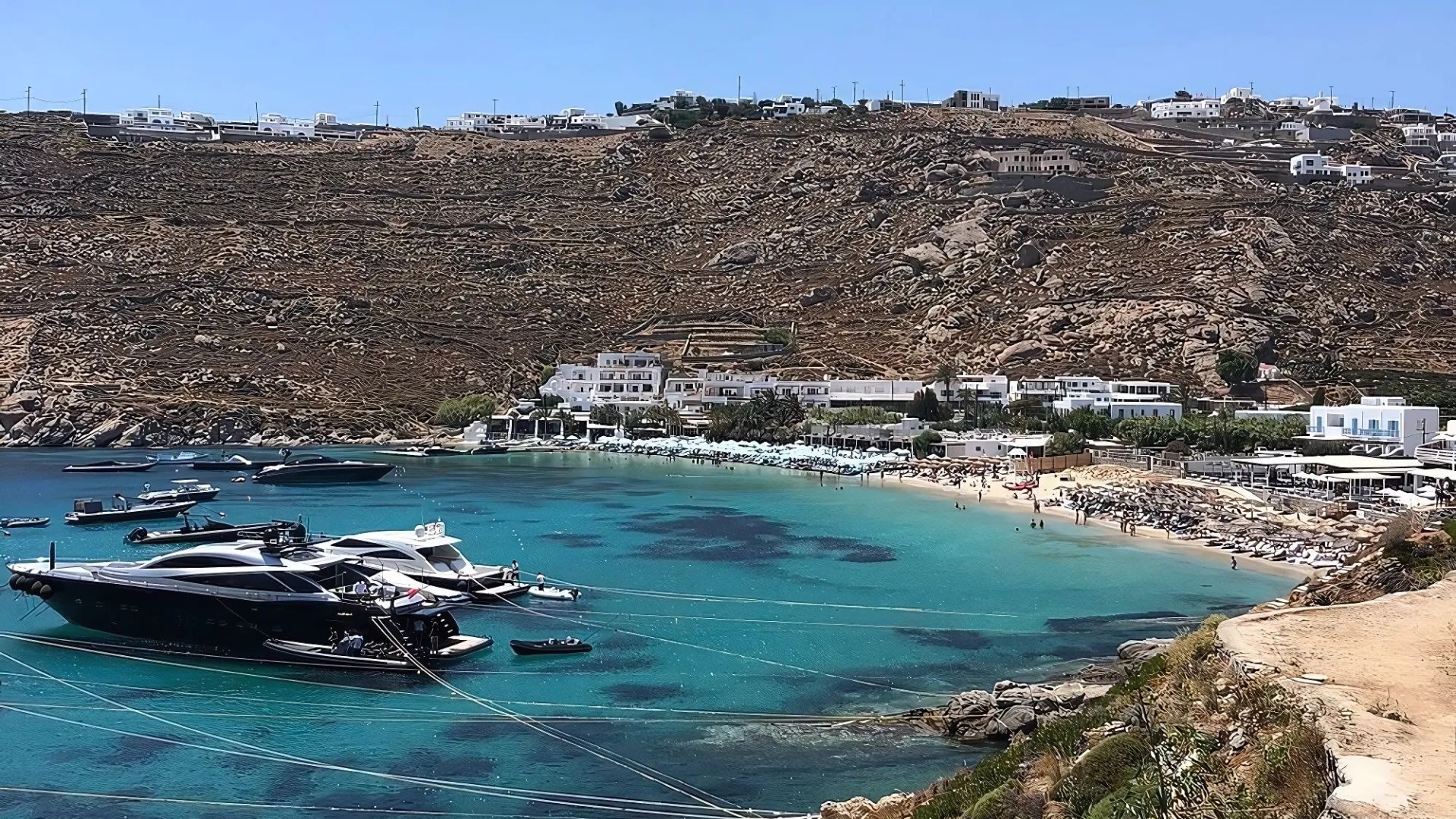 A scenic view of Psarou Beach in Mykonos, Greece, with clear turquoise waters and several boats anchored offshore