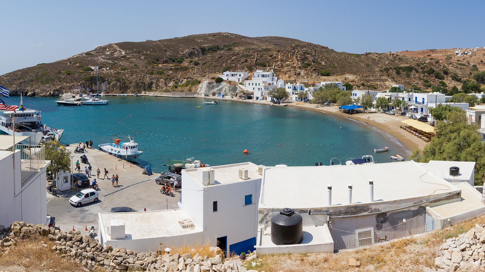 Scenic view of Psathi port in Kimolos, Greece, featuring white buildings, boats in the harbor, and a hillside backdrop.