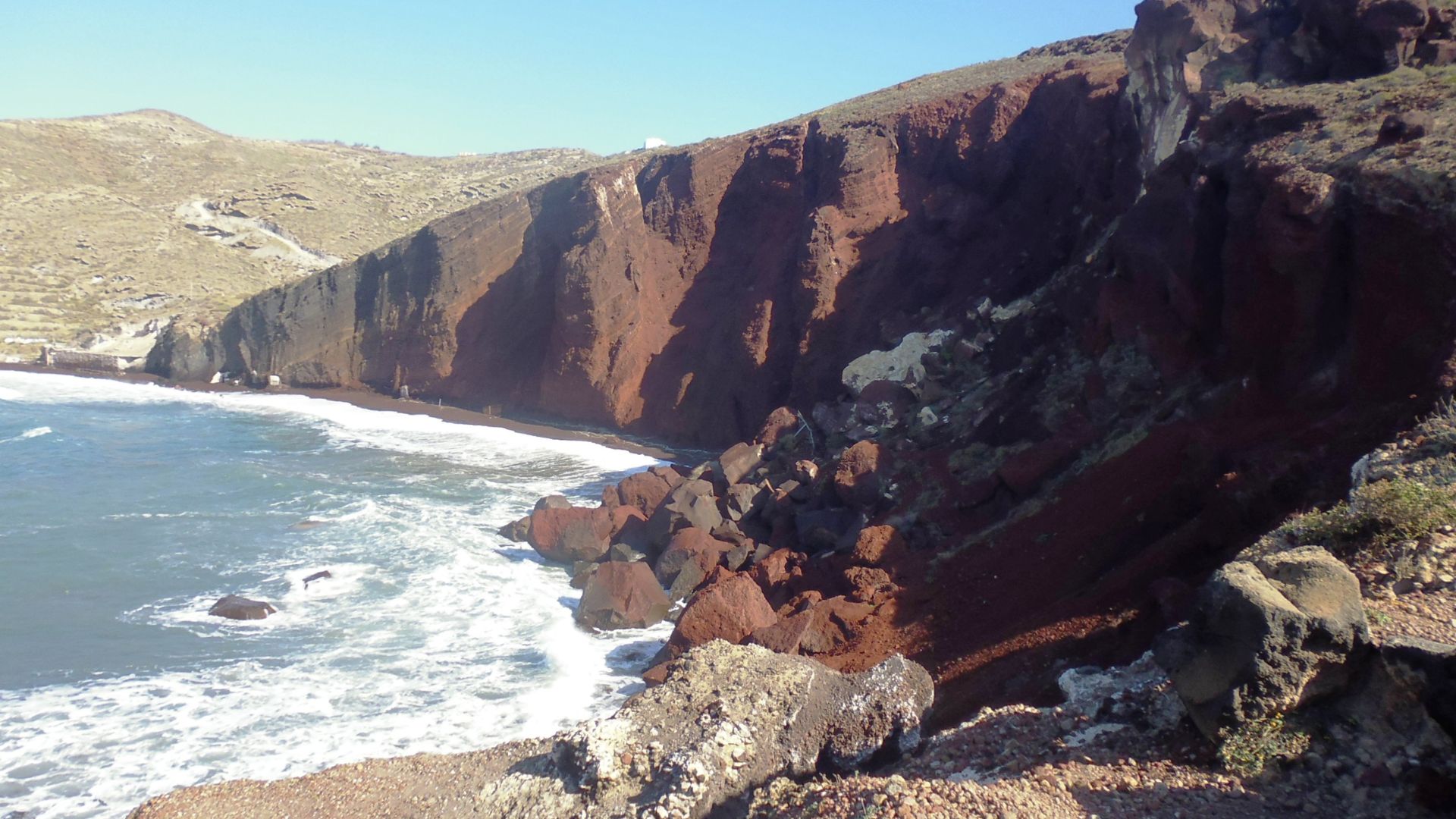 The rocky Red Beach in Santorini, Greece with red cliffs and blue water.