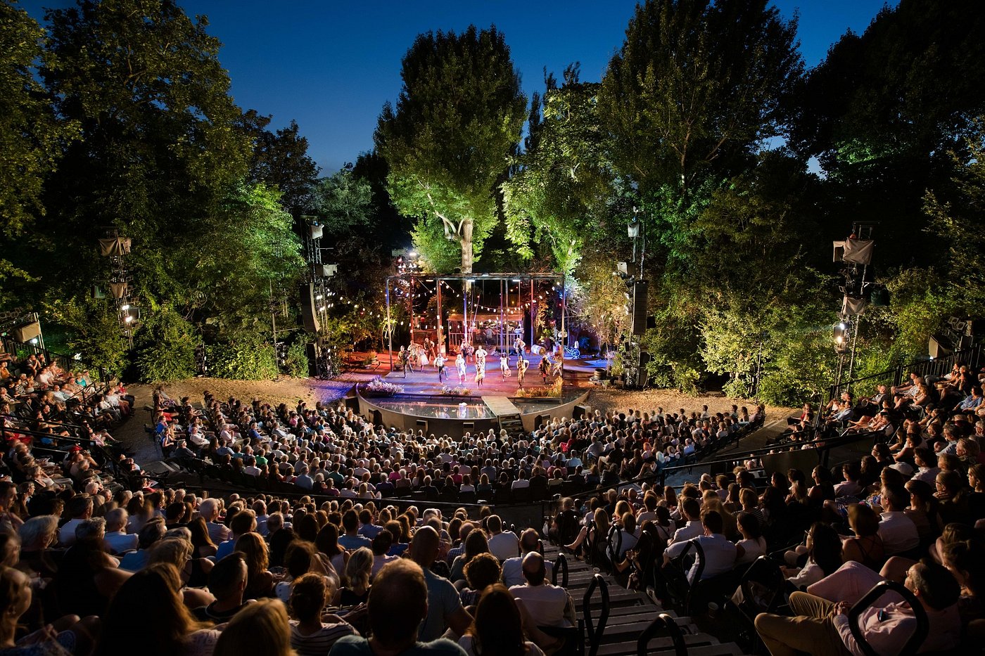 Night scene at Regent’s Park Open Air Theatre, with the stage illuminated and audience seated under the open sky