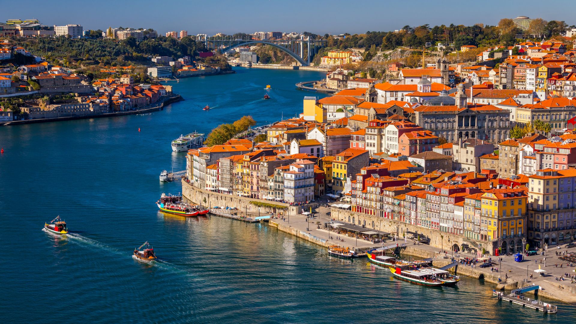 Aerial view of the colorful Ribeira district in Porto, Portugal, with historic buildings lining the Douro River and boats on the water.
