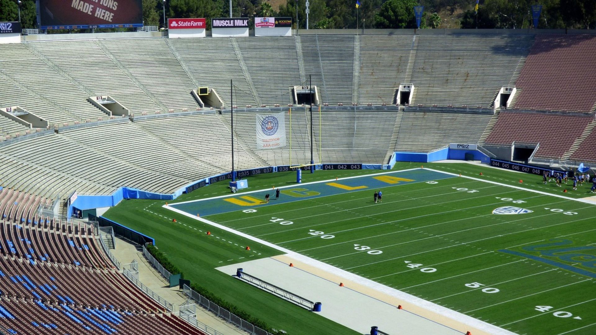 An aerial view of the Rose Bowl Stadium's football field and empty stands, with "CHAMPIONS MADE HERE" visible on a scoreboard.