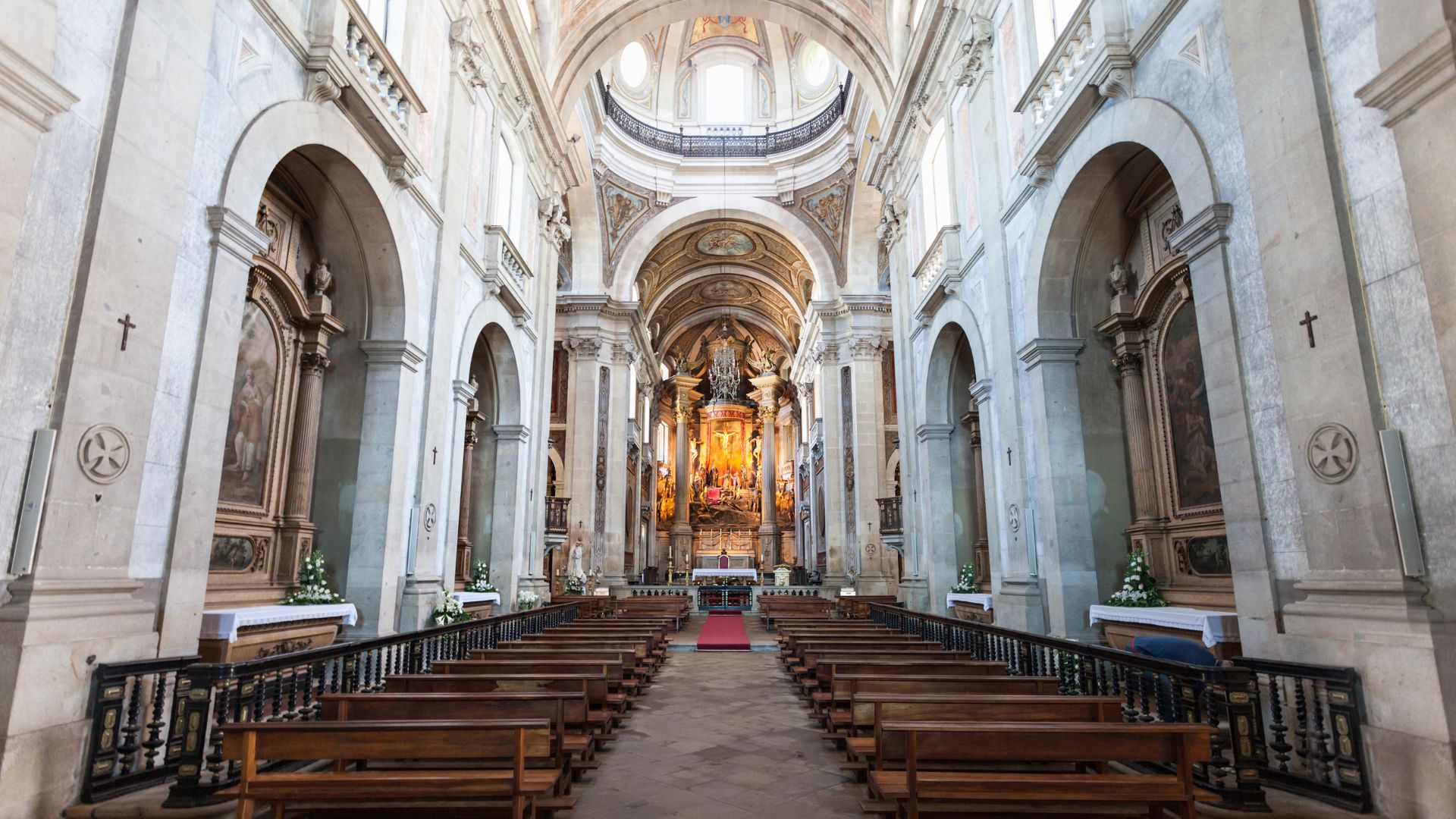 Interior view of the Basilica of Bom Jesus do Monte, showing rows of wooden pews leading towards a brightly lit altar.