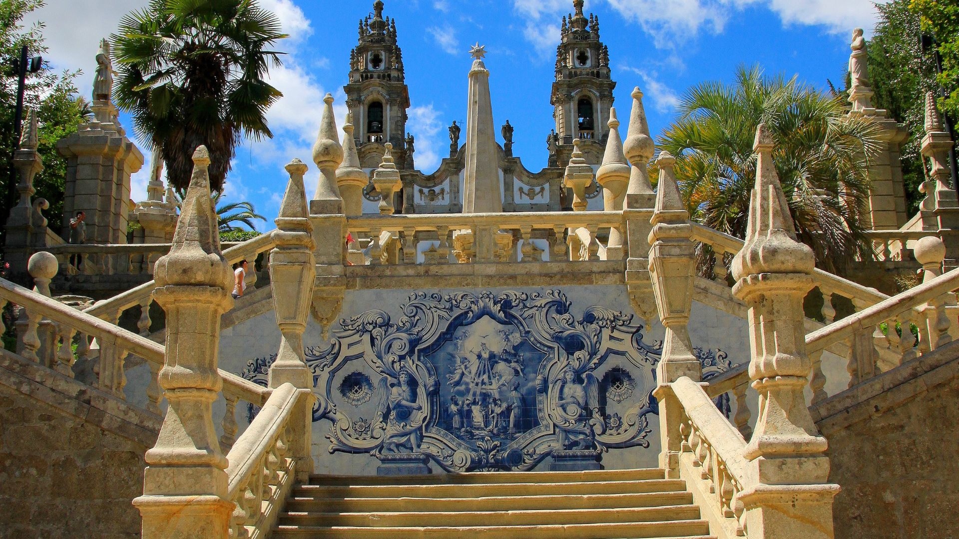 View of the Sanctuary of Nossa Senhora dos Remédios in Lamego, Portugal, showcasing its grand Baroque staircase with blue and white tilework, leading up to the church with its twin bell towers. The sanctuary is a popular pilgrimage site and a significant example of Baroque architecture.