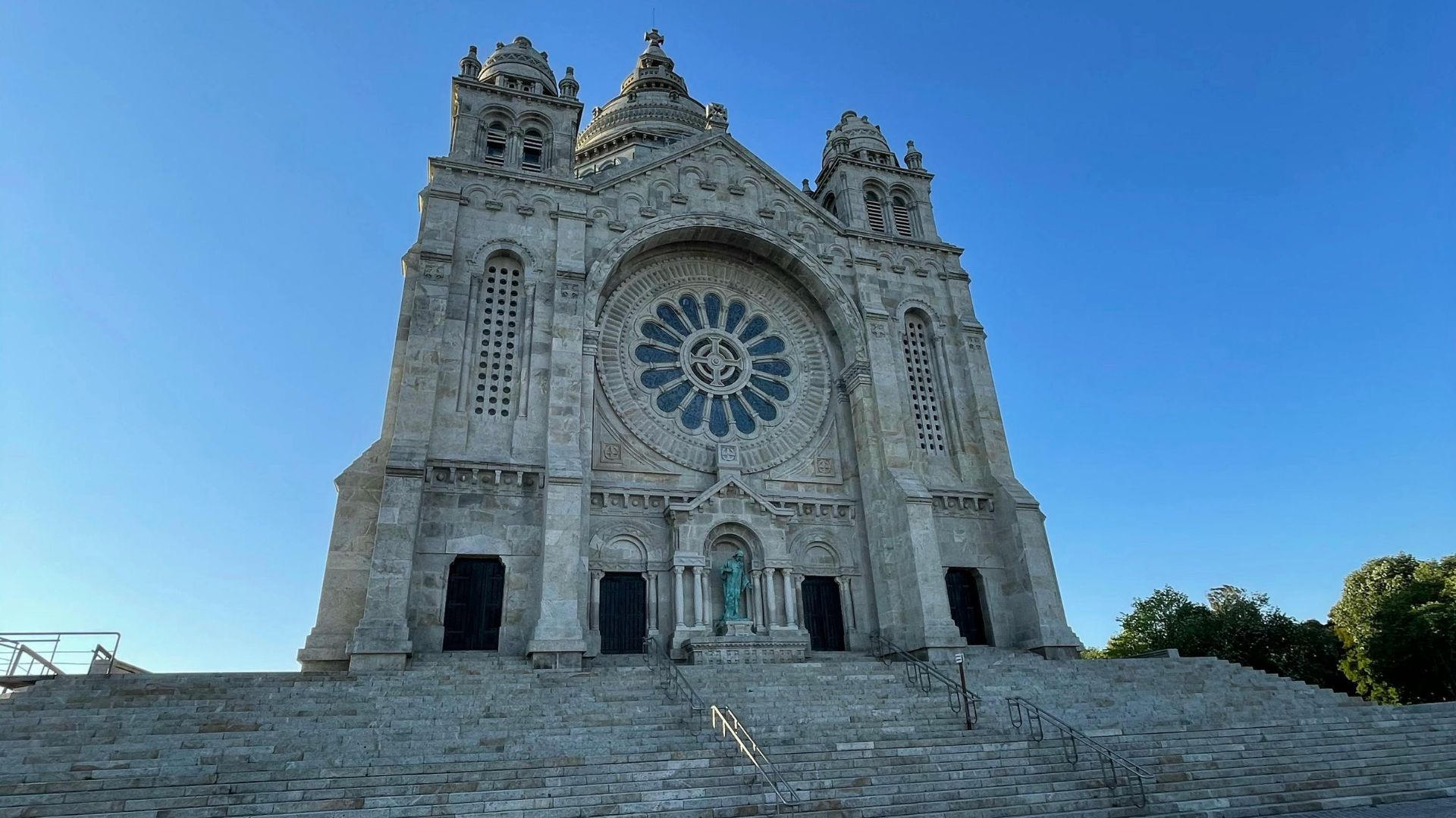 A grand stone sanctuary with a large rose window and imposing facade, set against a blue sky with clouds.