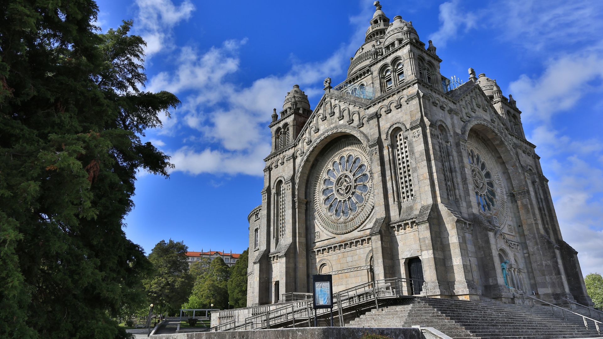 A grand stone sanctuary with a large rose window and imposing facade, set against a blue sky with clouds.