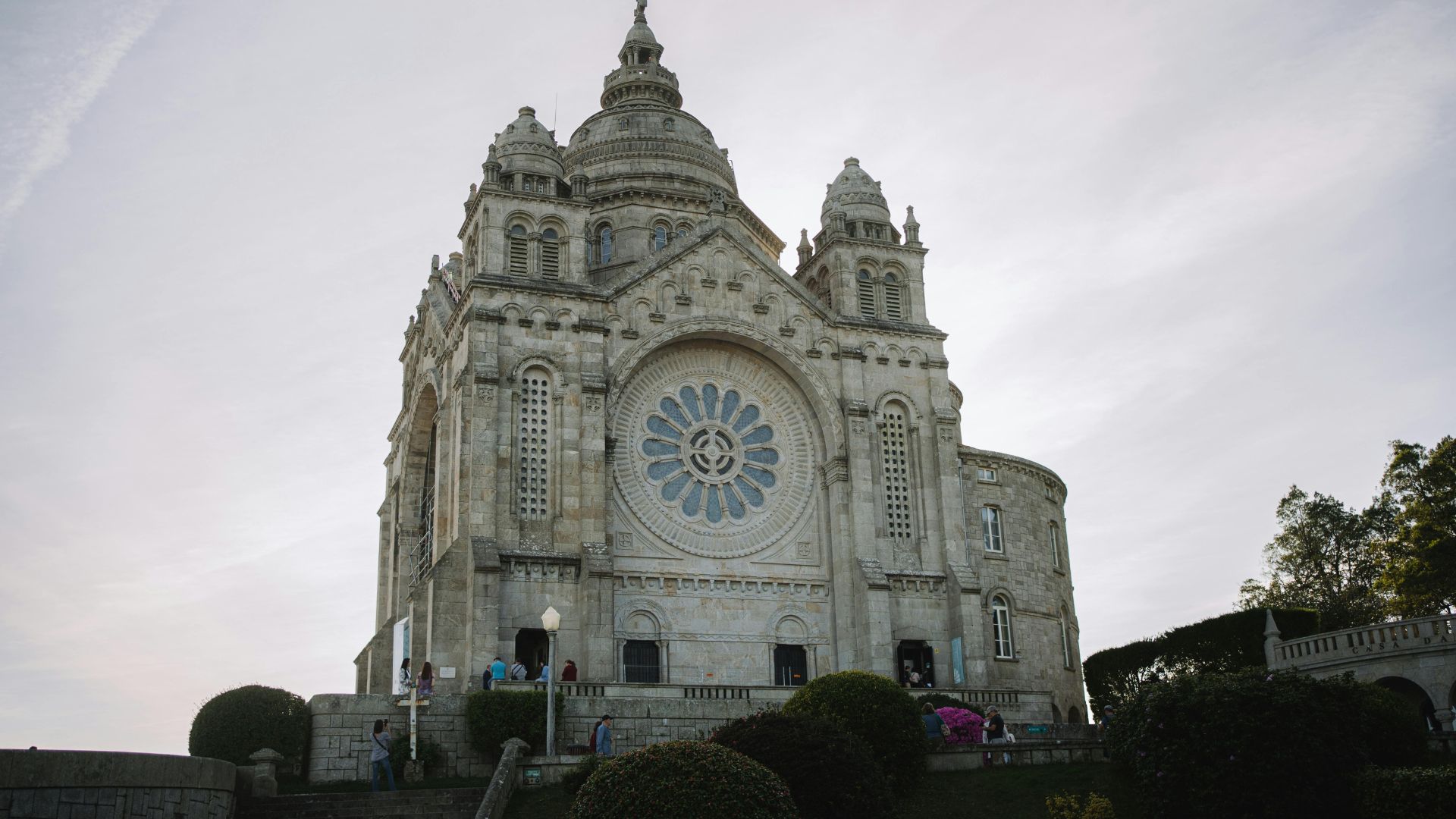 A grand stone sanctuary with a large rose window and imposing facade, set against a blue sky with clouds.