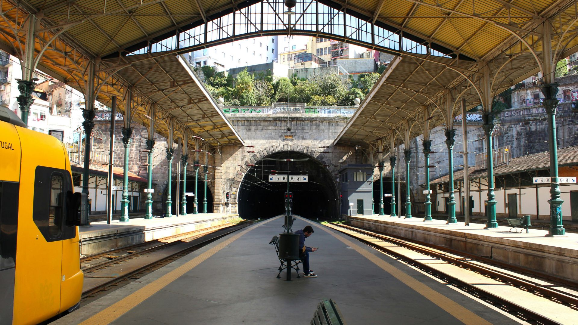 A yellow train and some passengers sitting at the bench at São Bento Railway Station in Porto, Portugal. 