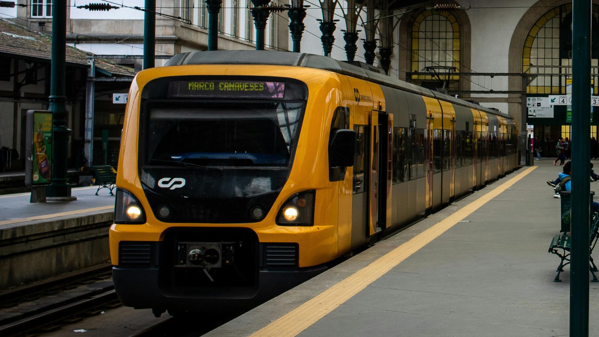 A yellow train and some passengers sitting at the bench at São Bento Railway Station in Porto, Portugal. 