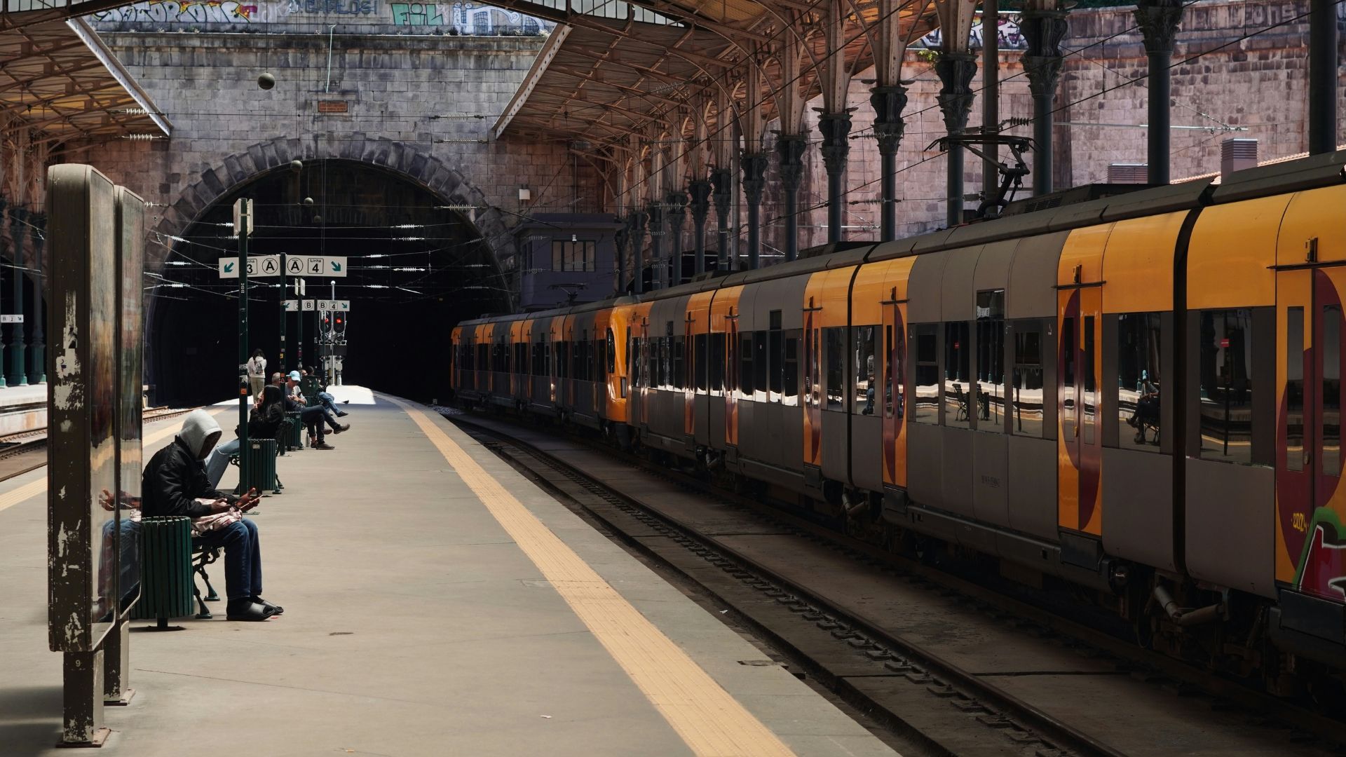 A yellow train and some passengers sitting at the bench at São Bento Railway Station in Porto, Portugal. 