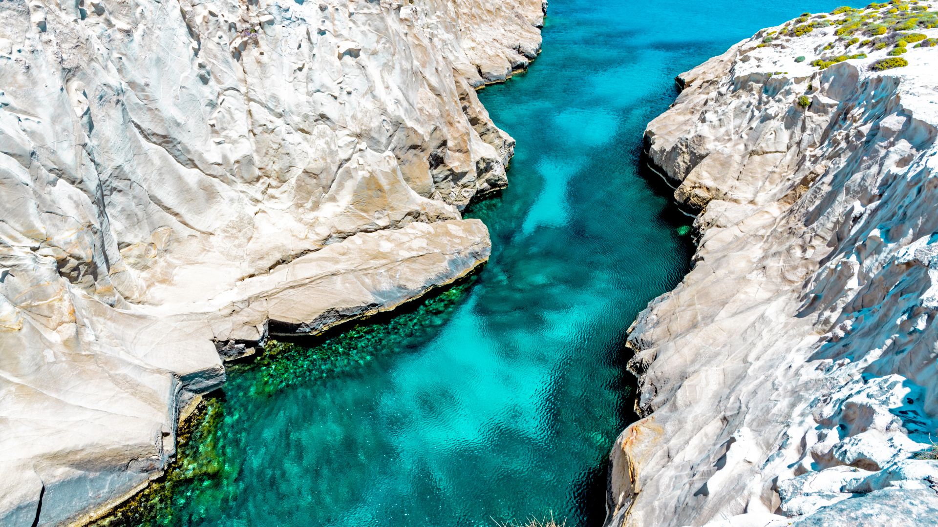 Sarakiniko Beach in Milos, Greece, features a unique lunar landscape of white volcanic rock formations against a backdrop of turquoise sea.