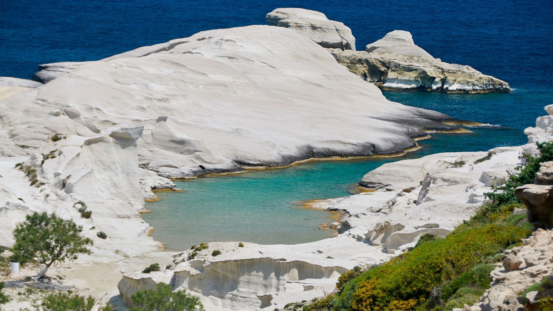 Sarakiniko Beach in Milos, Greece, features a unique lunar landscape of white volcanic rock formations against a backdrop of turquoise sea.