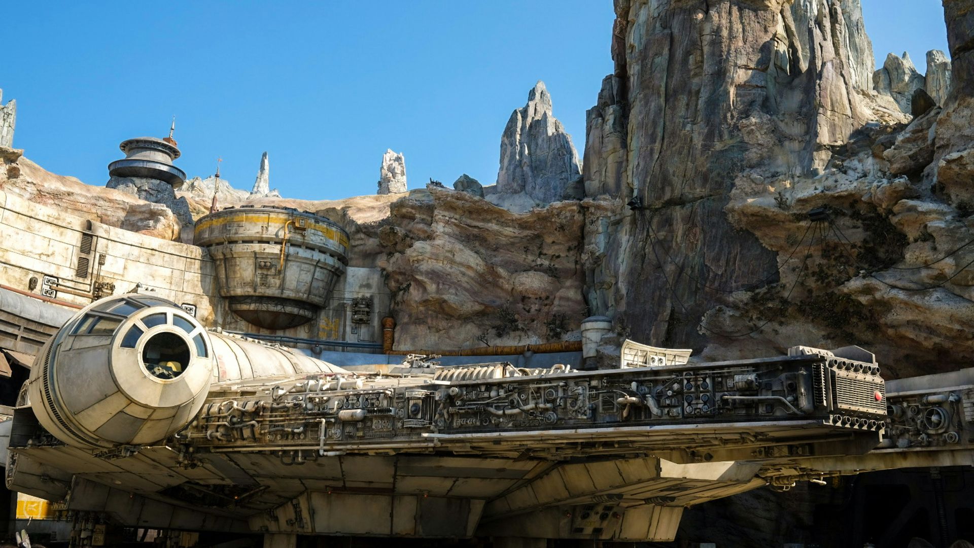 Millennium Falcon parked in front of towering rock formations at Star Wars: Galaxy's Edge in Disneyland Park, Anaheim, California, a popular theme park attraction.