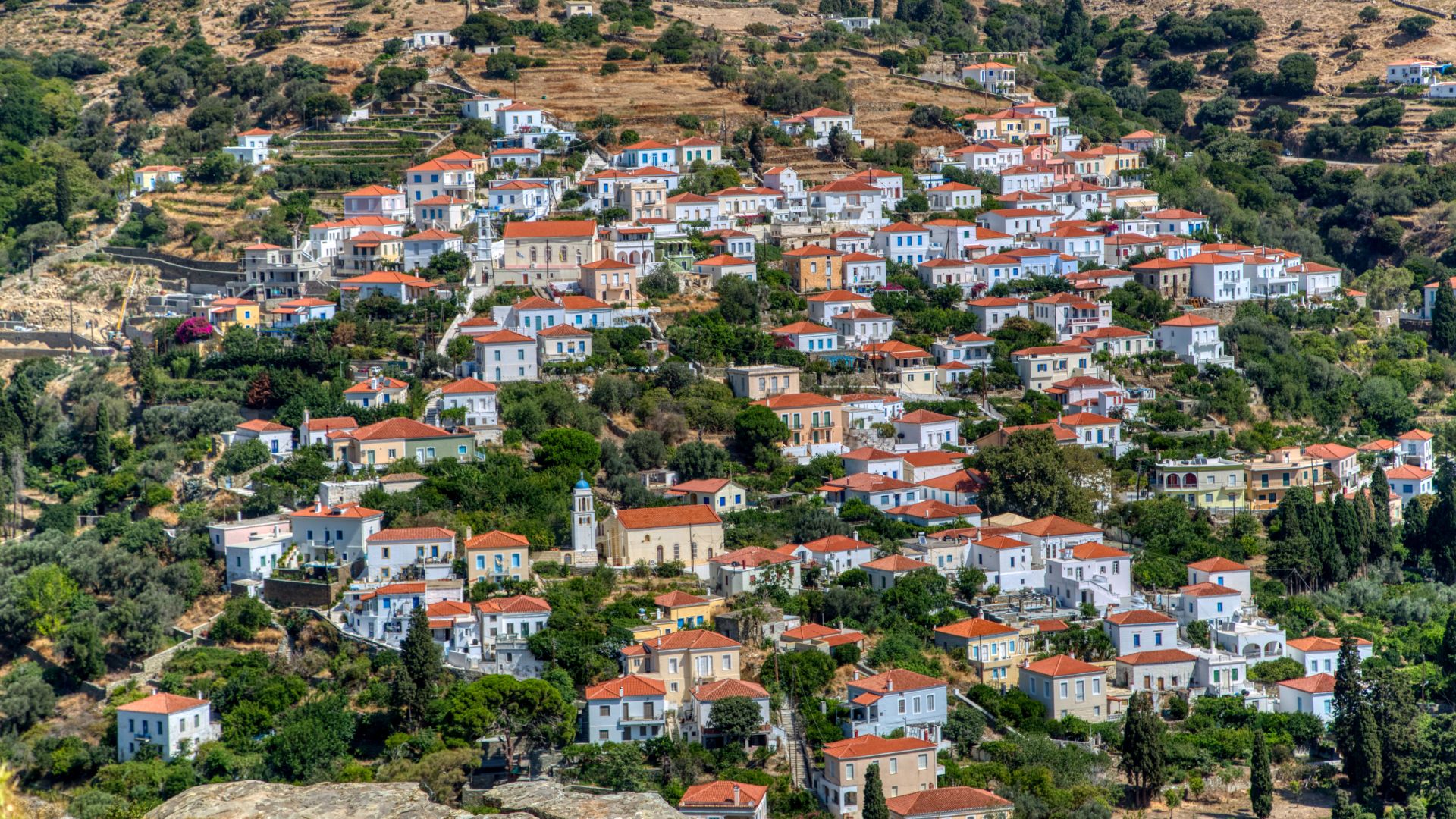 A high-angle shot of the village of Stenies in Andros, Greece, with traditional stone houses and a lush green setting.