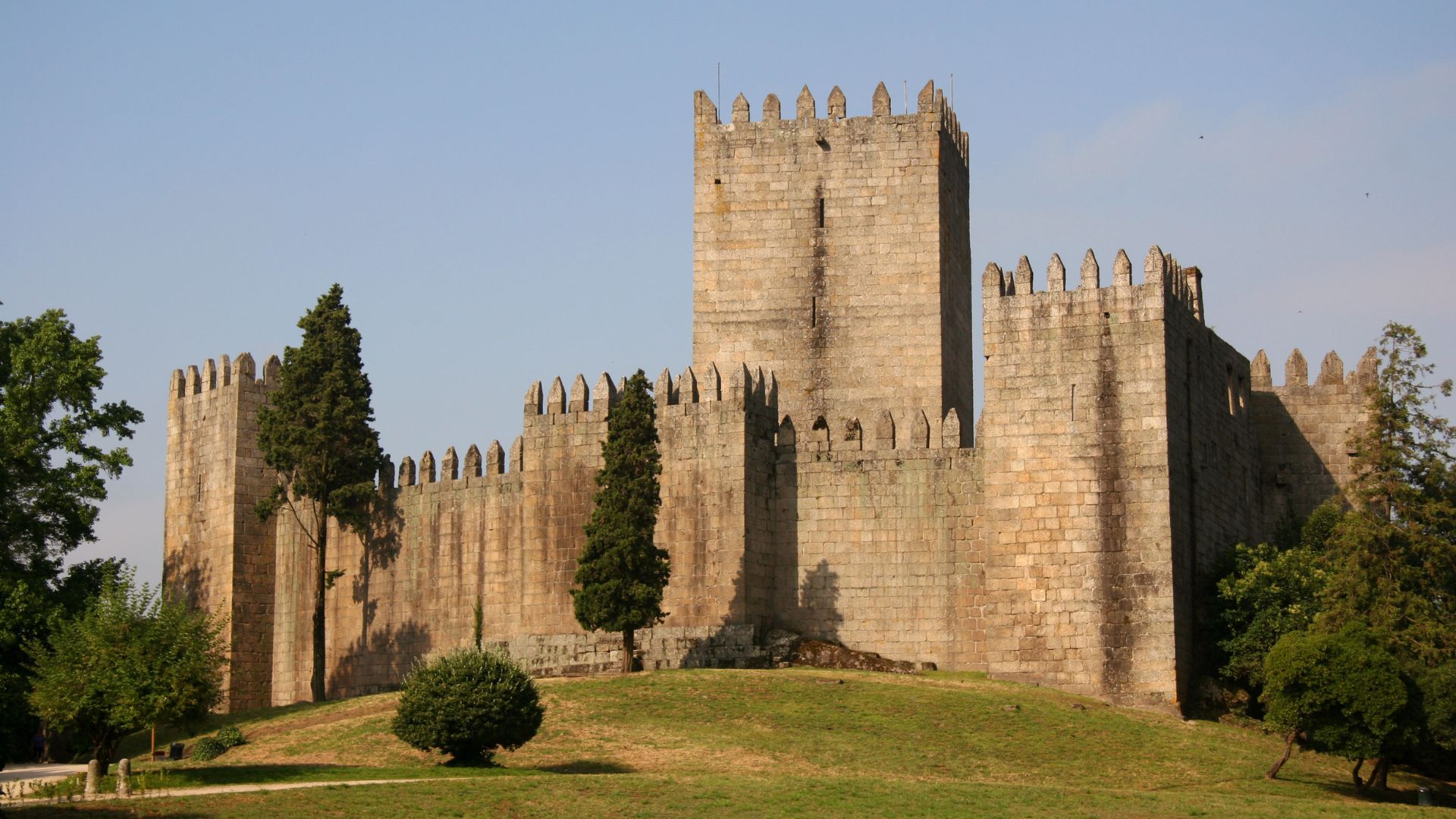 Guimarães Castle, a historic medieval fortress in Portugal's birthplace city of Guimarães, set against a clear sky and lush green landscape. Ideal for travel and history enthusiasts.