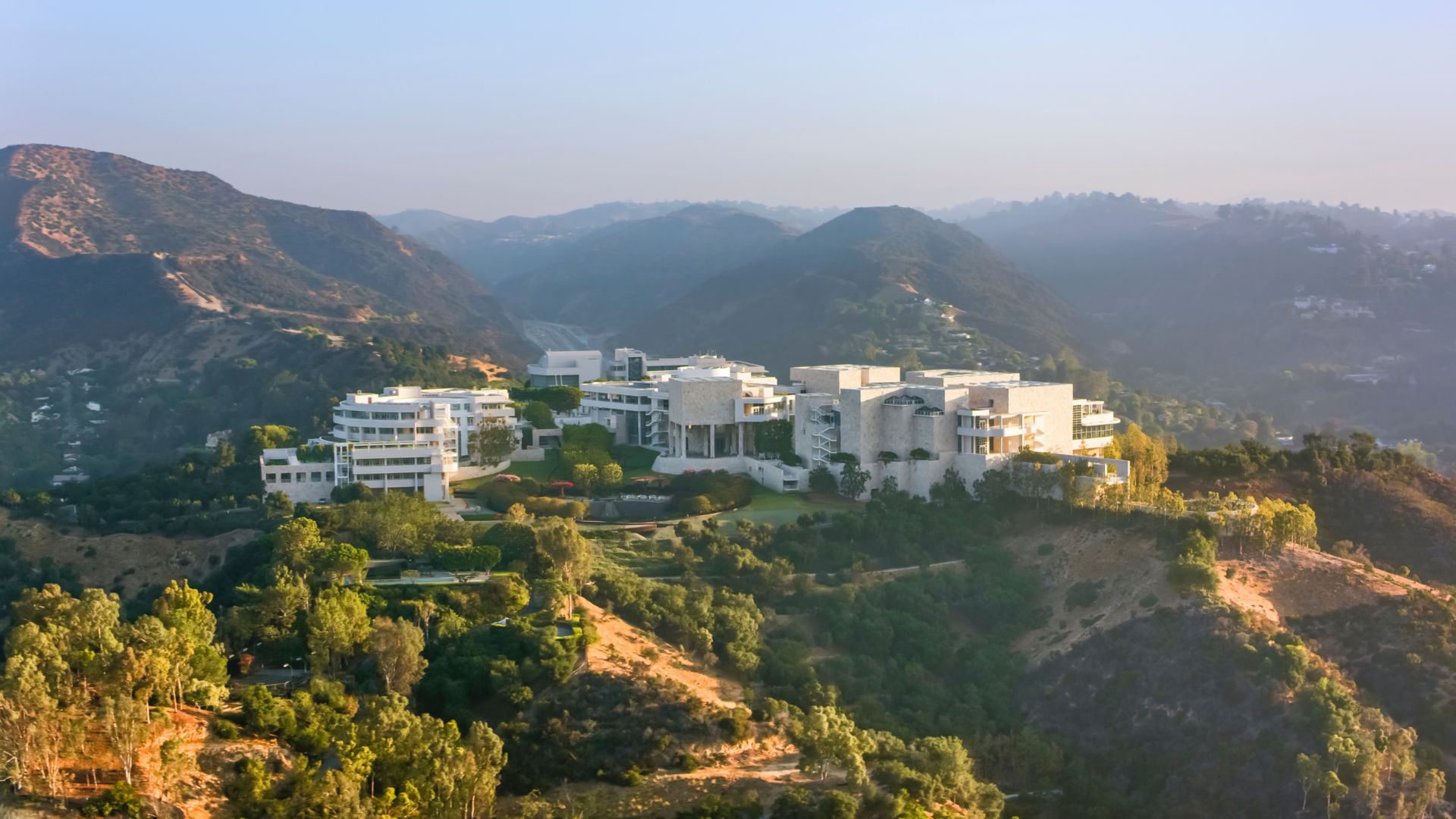 Aerial view of the Getty Center in Los Angeles, California, showcasing its modern architecture and sprawling complex nestled in the Santa Monica Mountains, with a highway winding through the landscape.