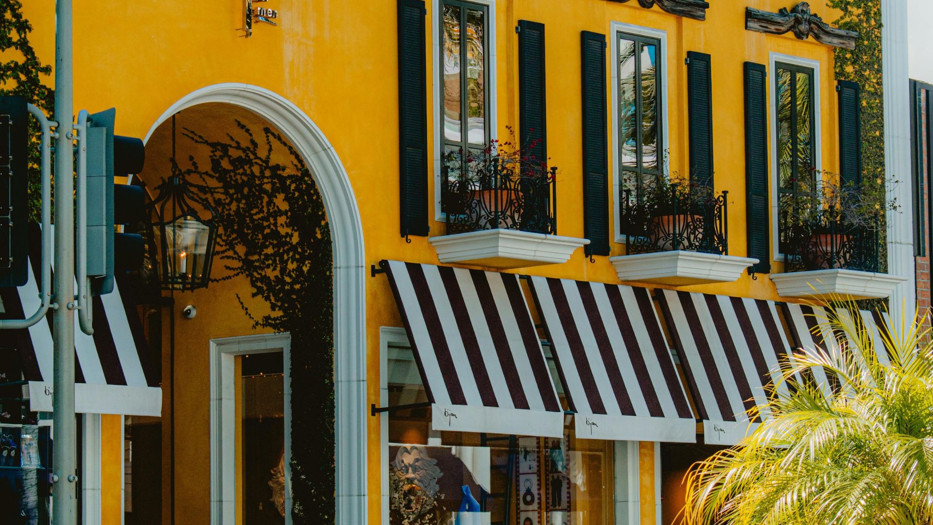 The iconic House of Bijan in Beverly Hills, California, featuring a yellow Mediterranean-style building and a matching yellow Rolls Royce parked outside. 