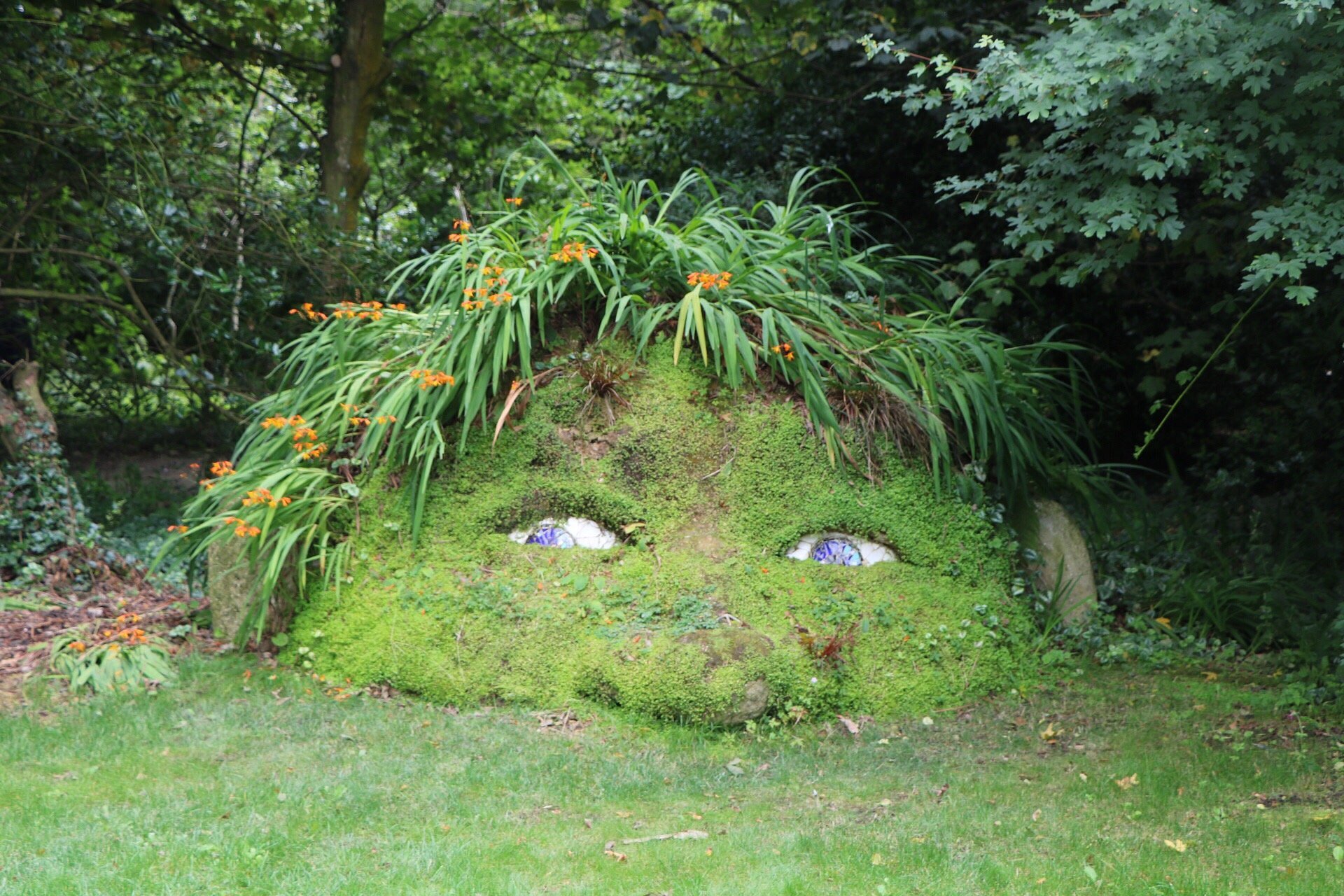 The Giant’s Head sculpture at the Lost Gardens of Heligan, with moss-covered stone eyes peering through a face formed from the surrounding greenery