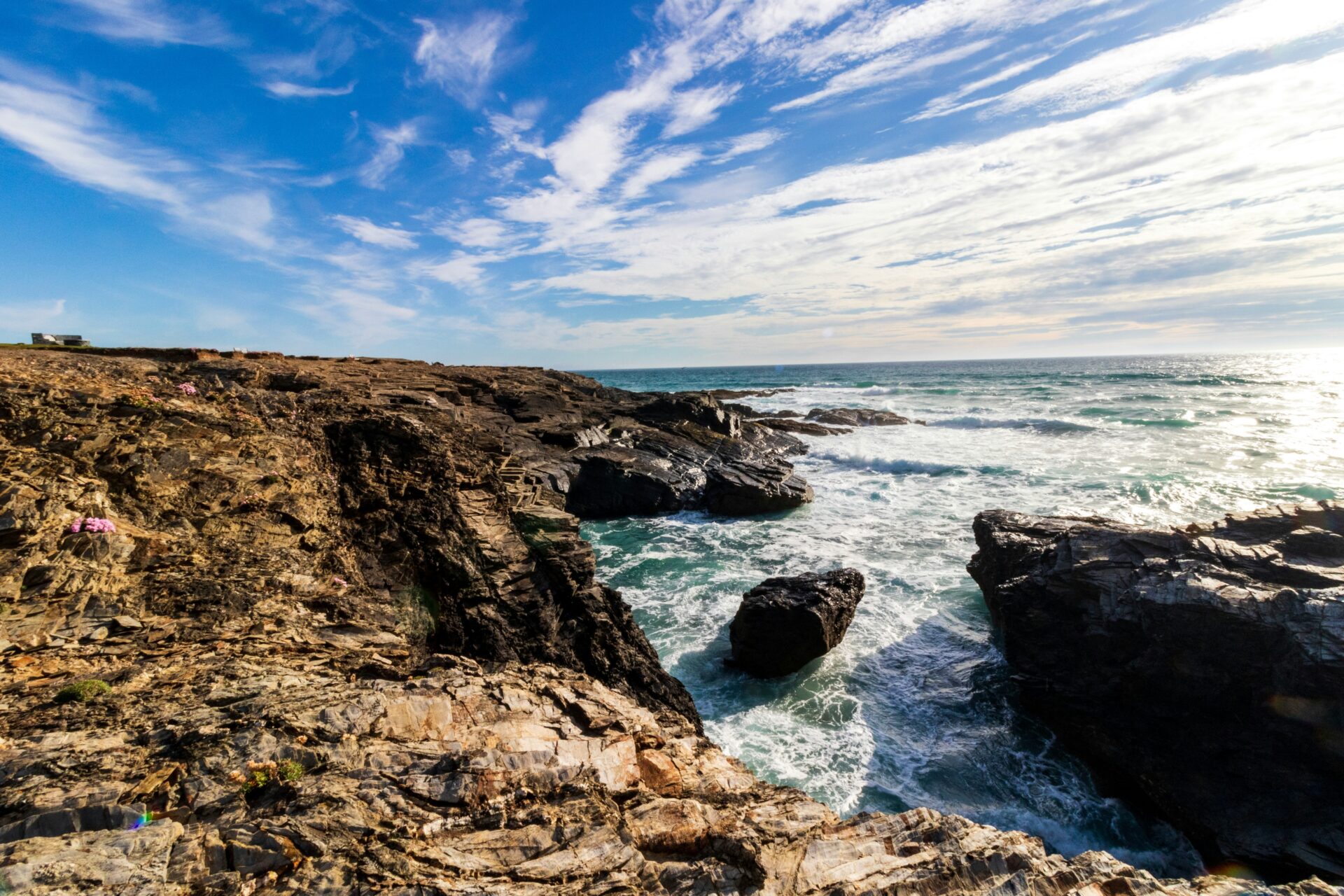 The rugged coastline of Padstow, with dramatic cliffs, scattered rocks, and foamy waves breaking along the shore,
