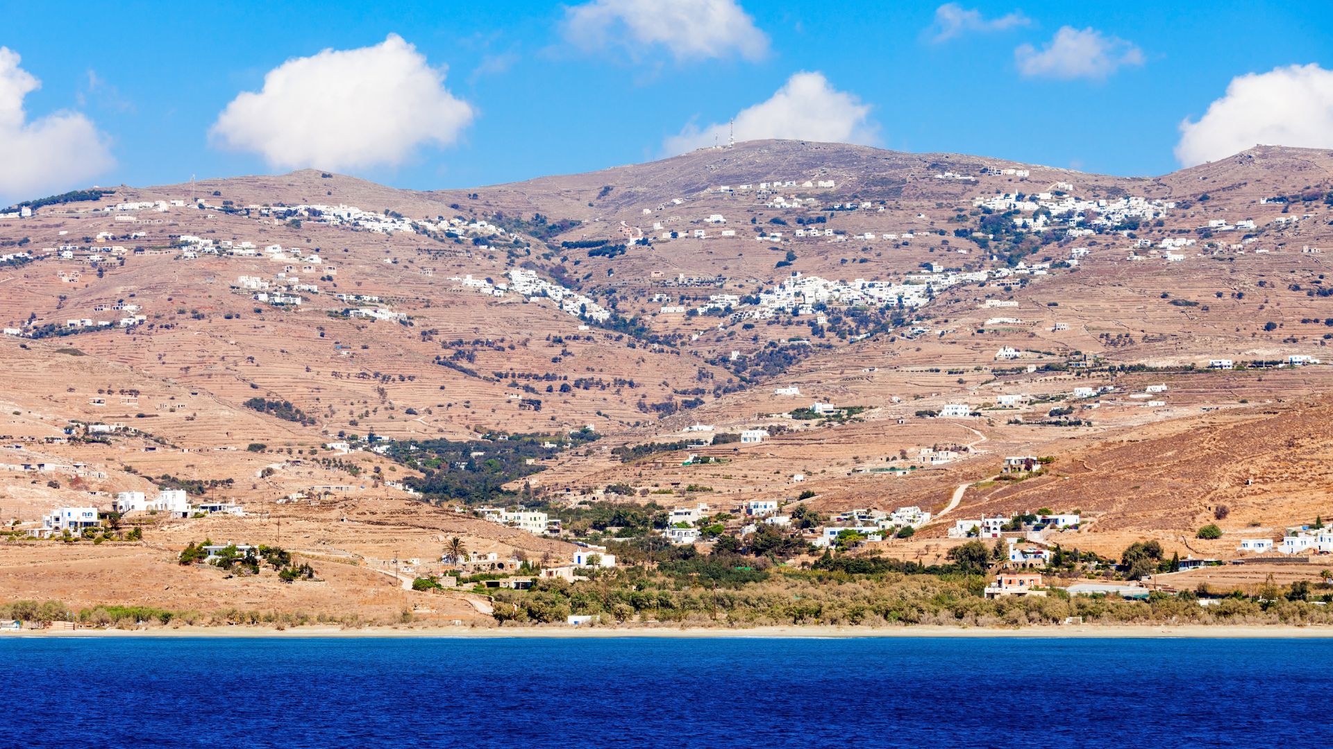 A hillside village on Tinos Island, Greece, with white houses and a deep blue sea.