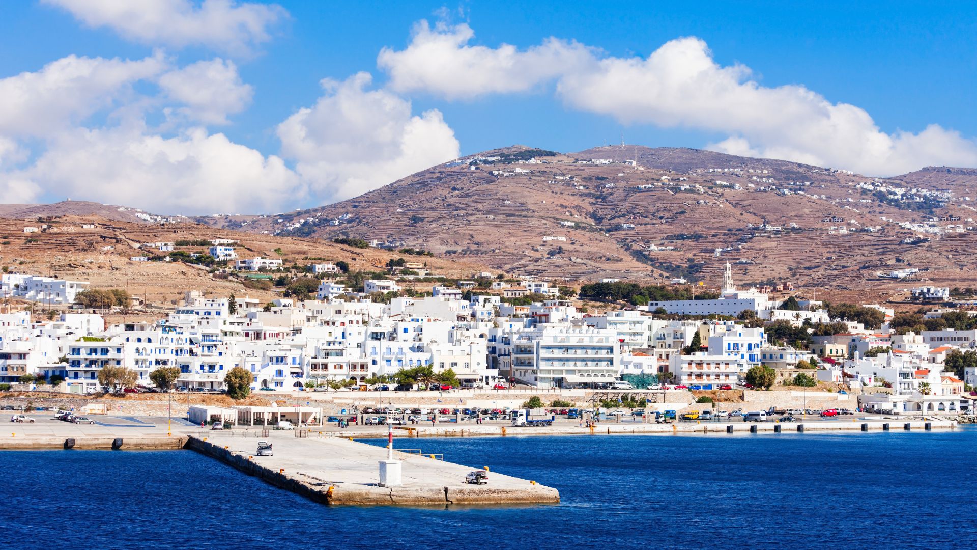 Tinos Town harbor with whitewashed buildings and a mountainous backdrop.