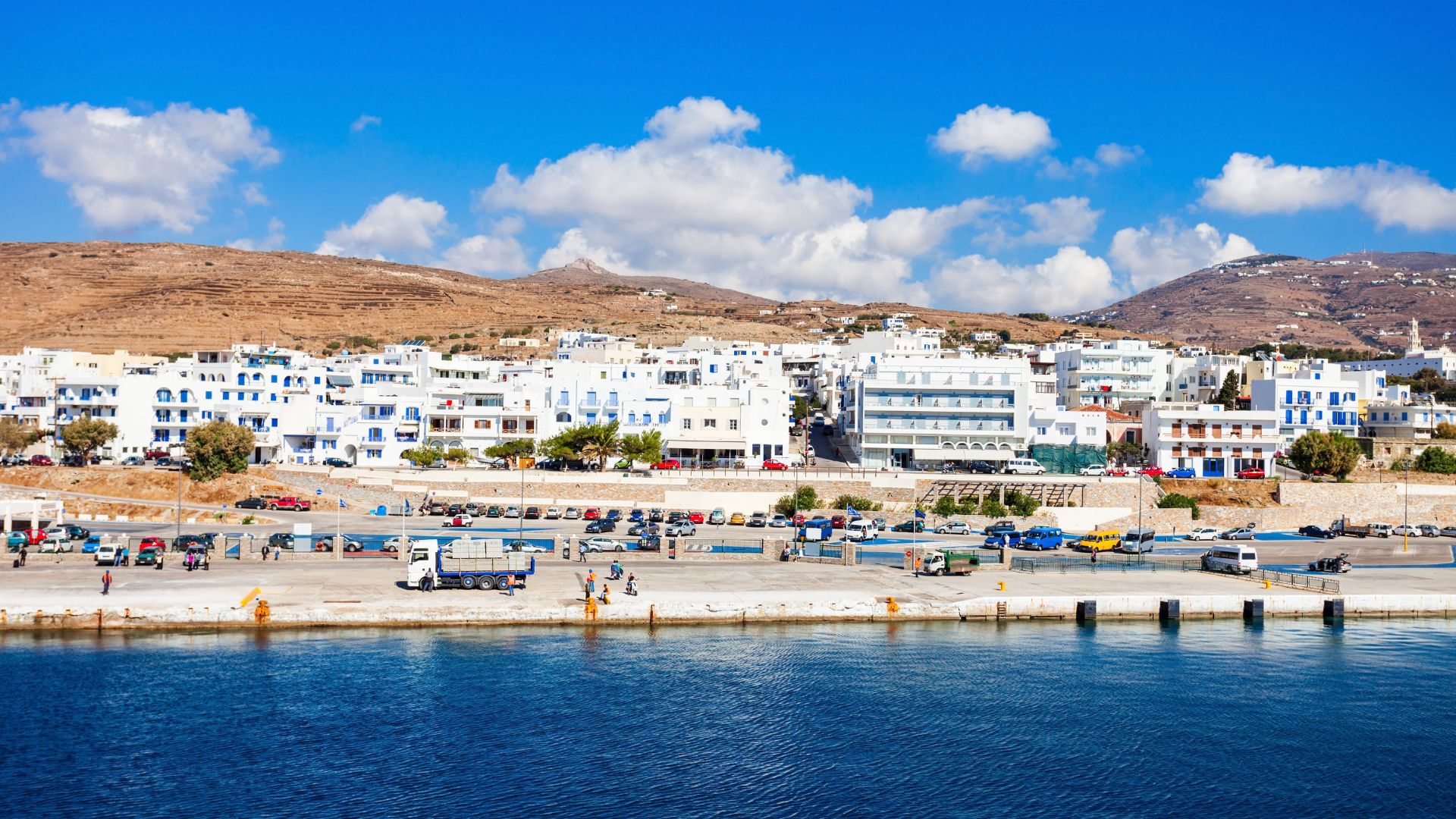 Tinos Town harbor with whitewashed buildings and a mountainous backdrop.