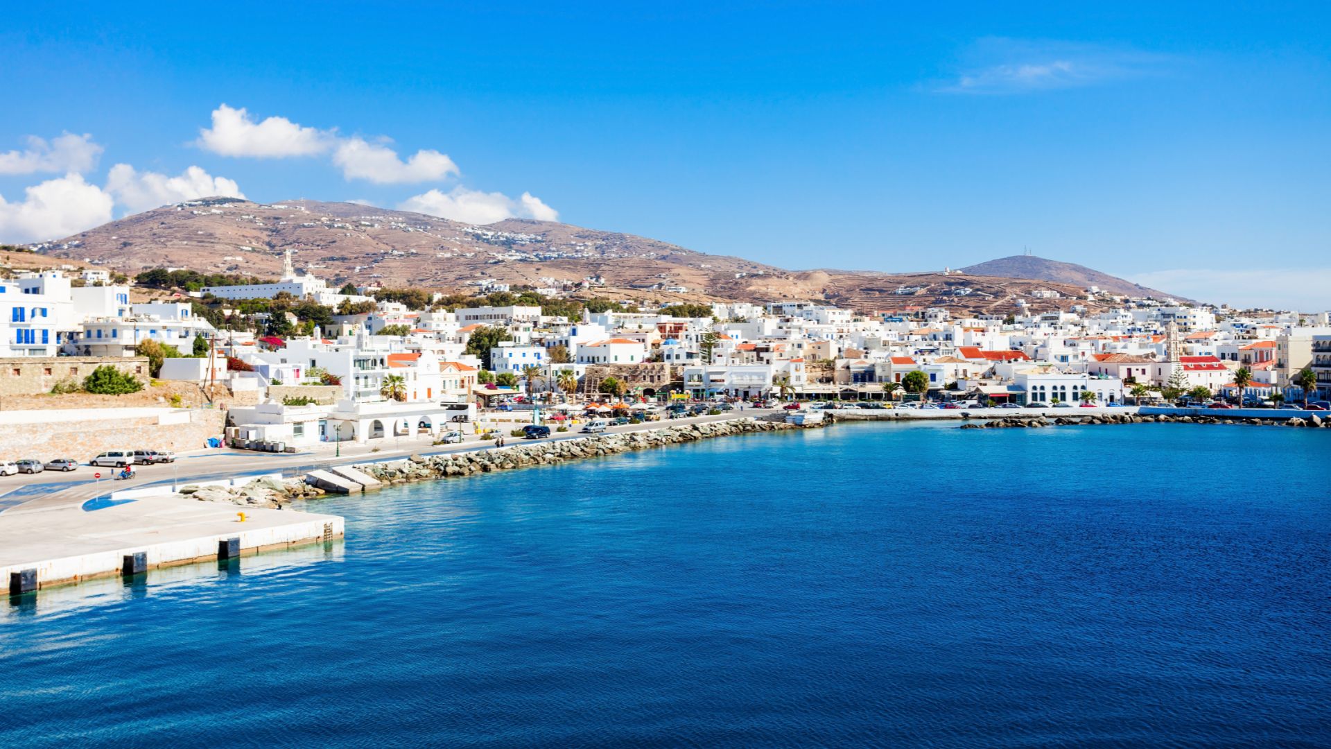 View of the port in Tinos Town, Greece, with white buildings and a harbor.
