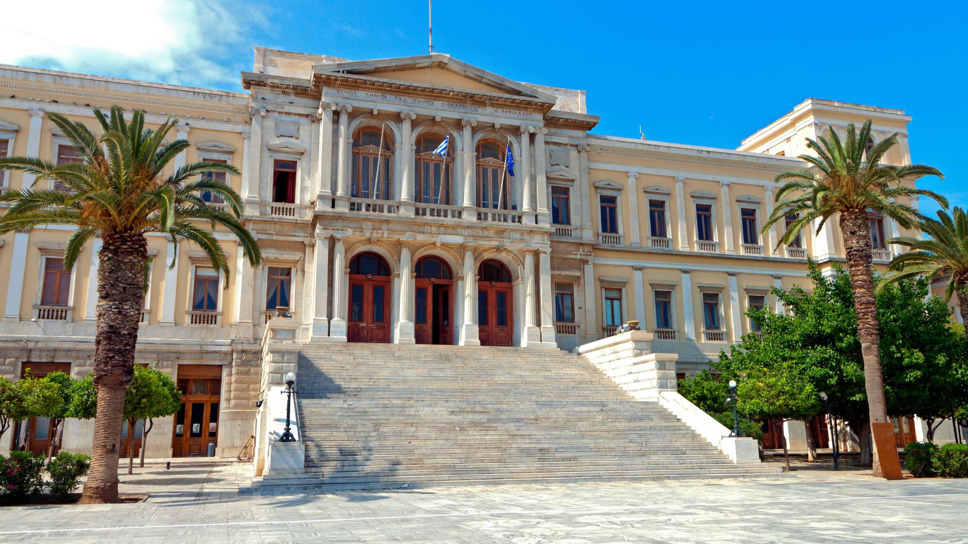 Neoclassical City Hall in Ermoupolis, Syros, Greece, with grand steps and palm trees.