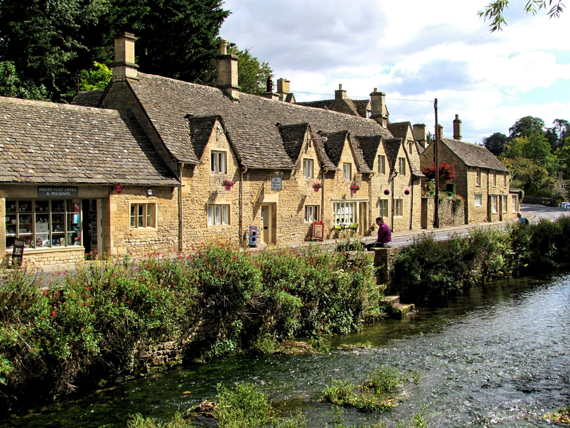 Traditional honey-colored stone cottages with steeply pitched roofs along a quiet lane in a Cotswold village