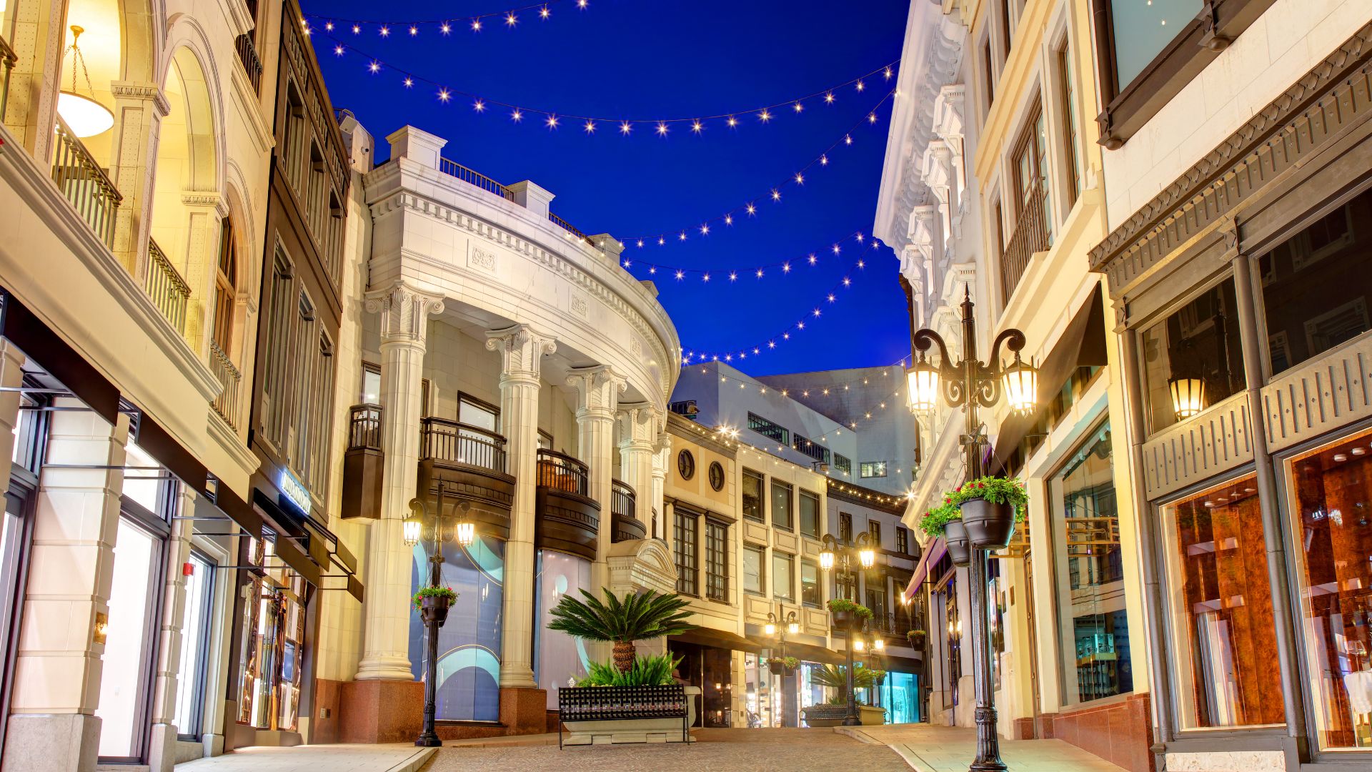 Night view of Two Rodeo Drive in Beverly Hills, California, showcasing its luxurious architecture, string lights, and upscale shopping environment.