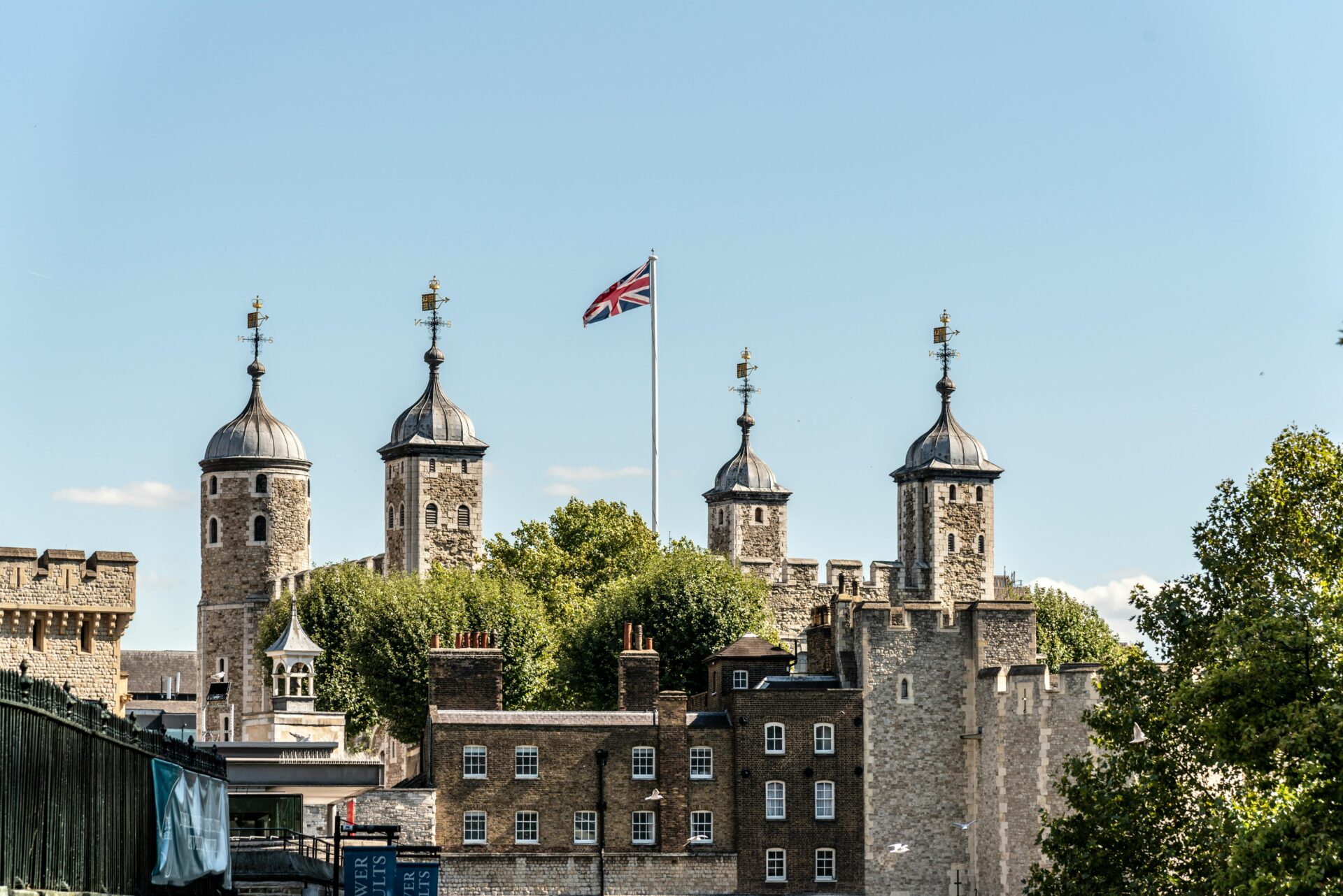 United Kingdom flag fluttering atop a flagpole, set against the iconic stone walls and turrets of the Tower of London