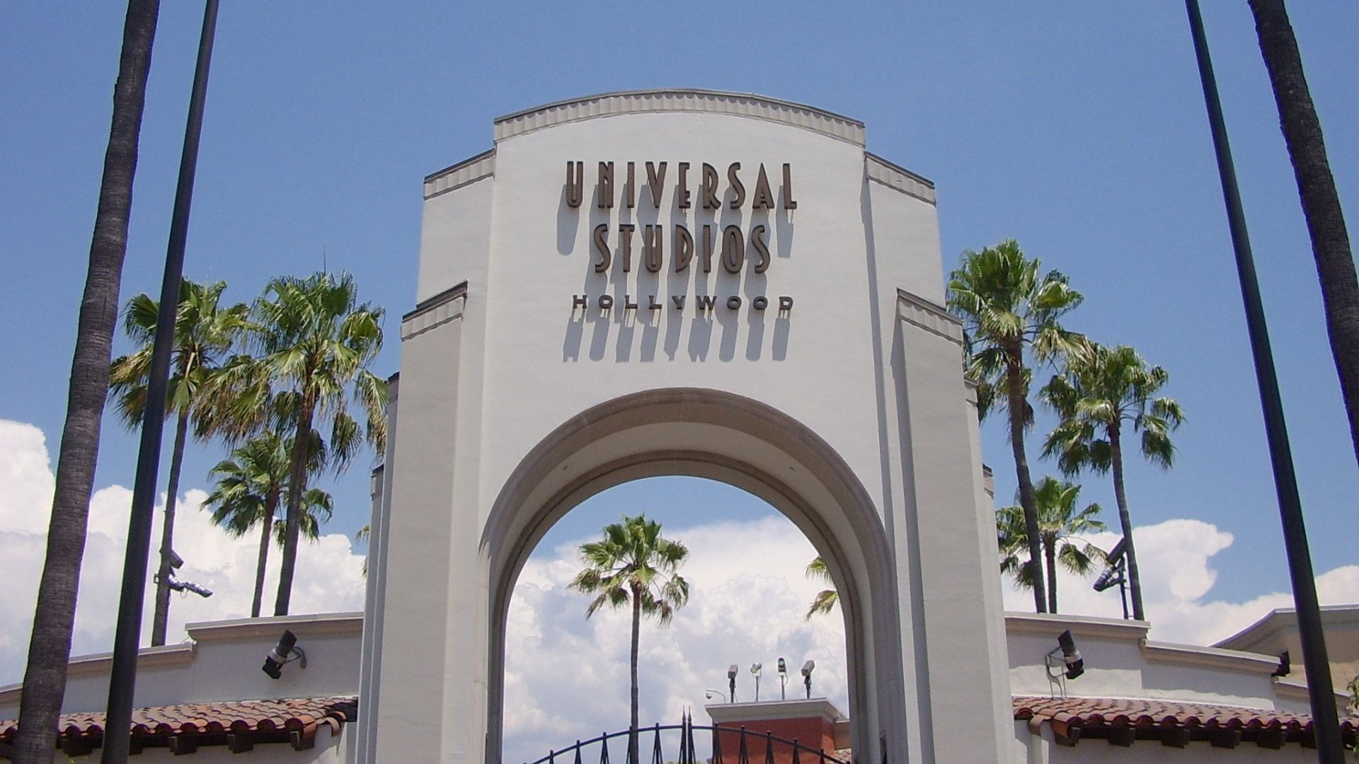 The grand entrance to Universal Studios Hollywood, featuring the iconic archway with the Universal Studios Hollywood logo, palm trees, and a bright blue sky, inviting visitors into a world of movie magic.
