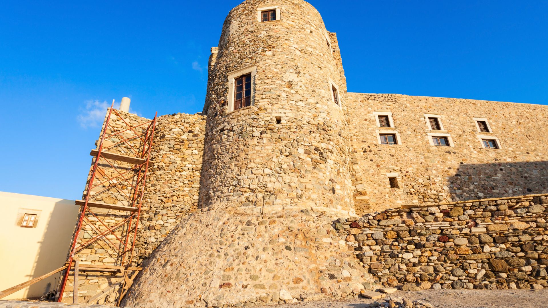 A stone castle with a round tower, scaffolding on one side, and a small gate of Venetian Castle of Naxos (Kastro Castle) in Naxos, Greece.