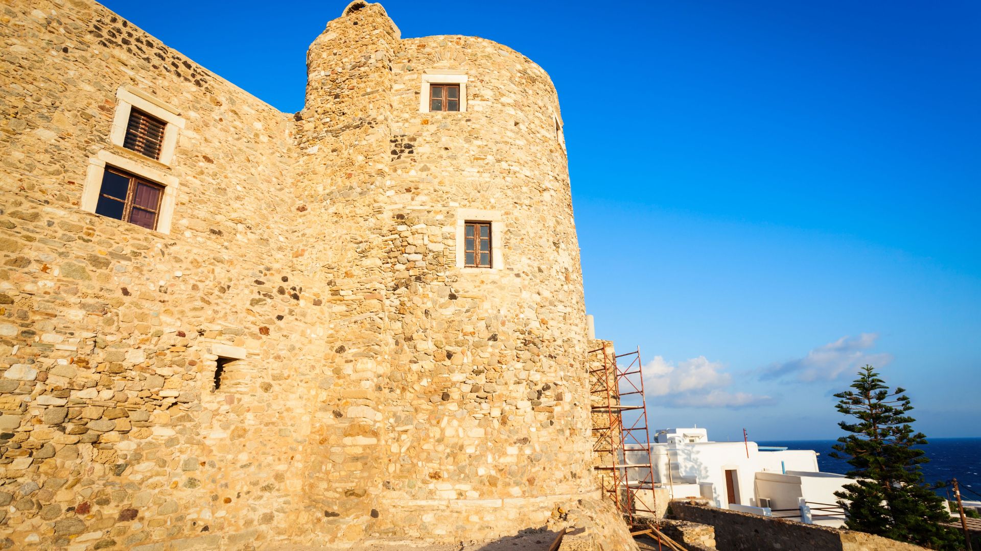 A stone castle with a round tower, scaffolding on one side, and a small gate of Venetian Castle of Naxos (Kastro Castle) in Naxos, Greece.
