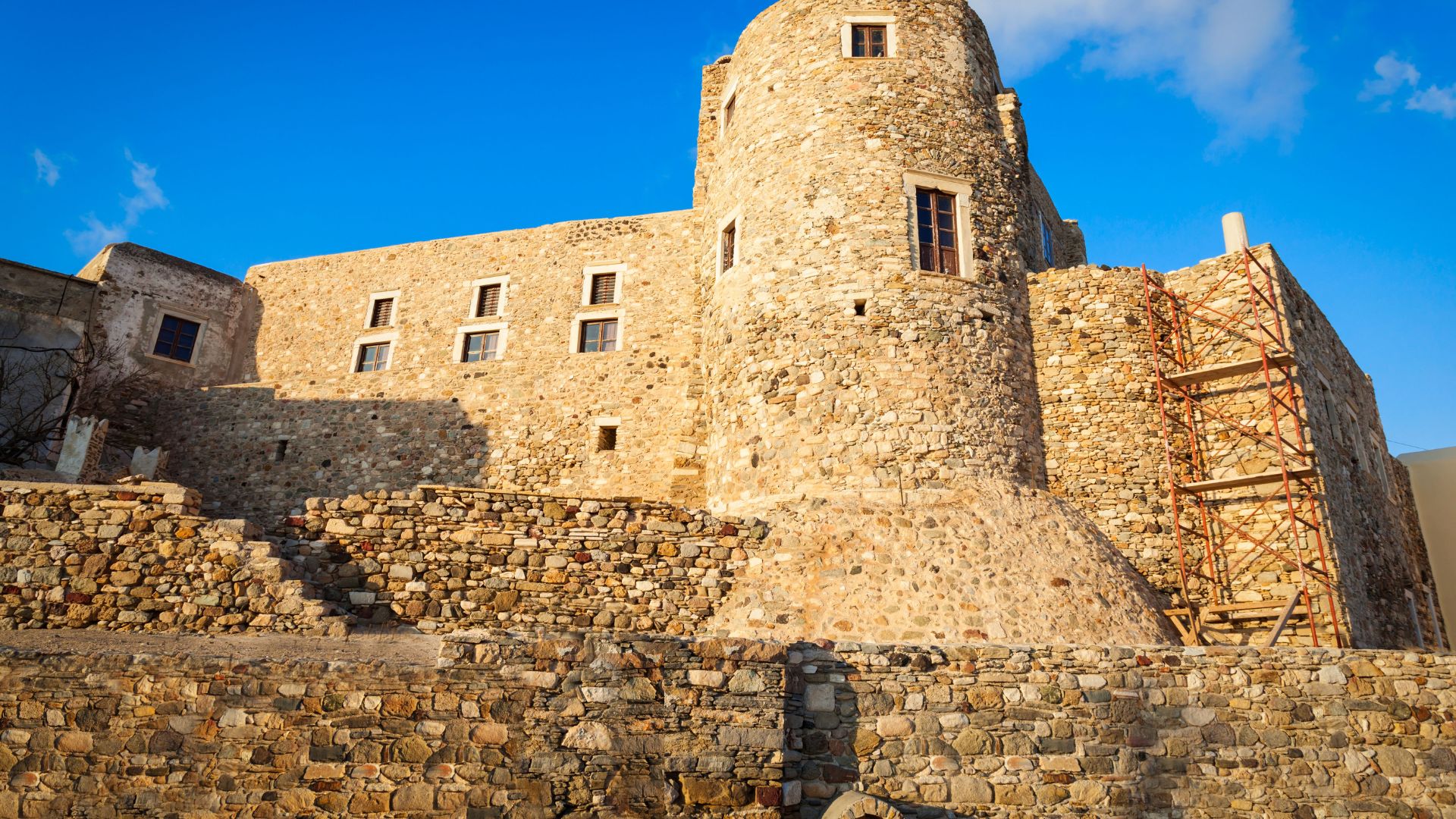 A stone castle with a round tower, scaffolding on one side, and a small gate of Venetian Castle of Naxos (Kastro Castle) in Naxos, Greece.