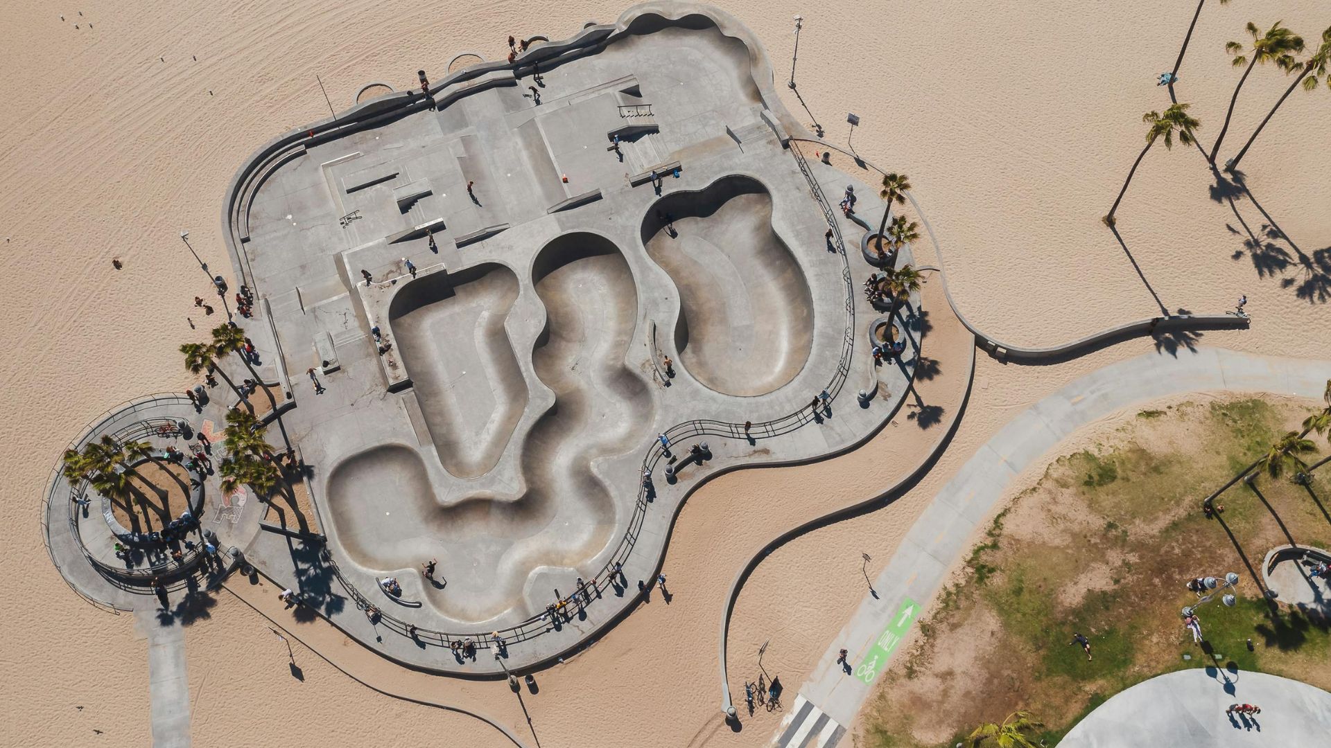 Aerial view of the iconic Venice Beach Skatepark in Los Angeles, California, showcasing its concrete bowls, ramps, and rails on the sandy beachfront, surrounded by palm trees and the boardwalk, ideal for skateboarding and action sports enthusiasts.