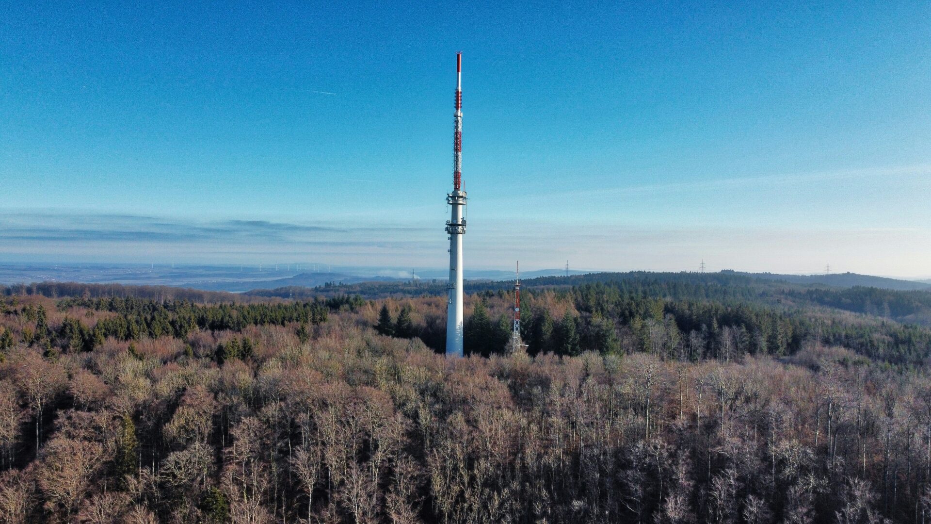 White and red tower standing in an open green grass field under a bright blue sky near Aalen