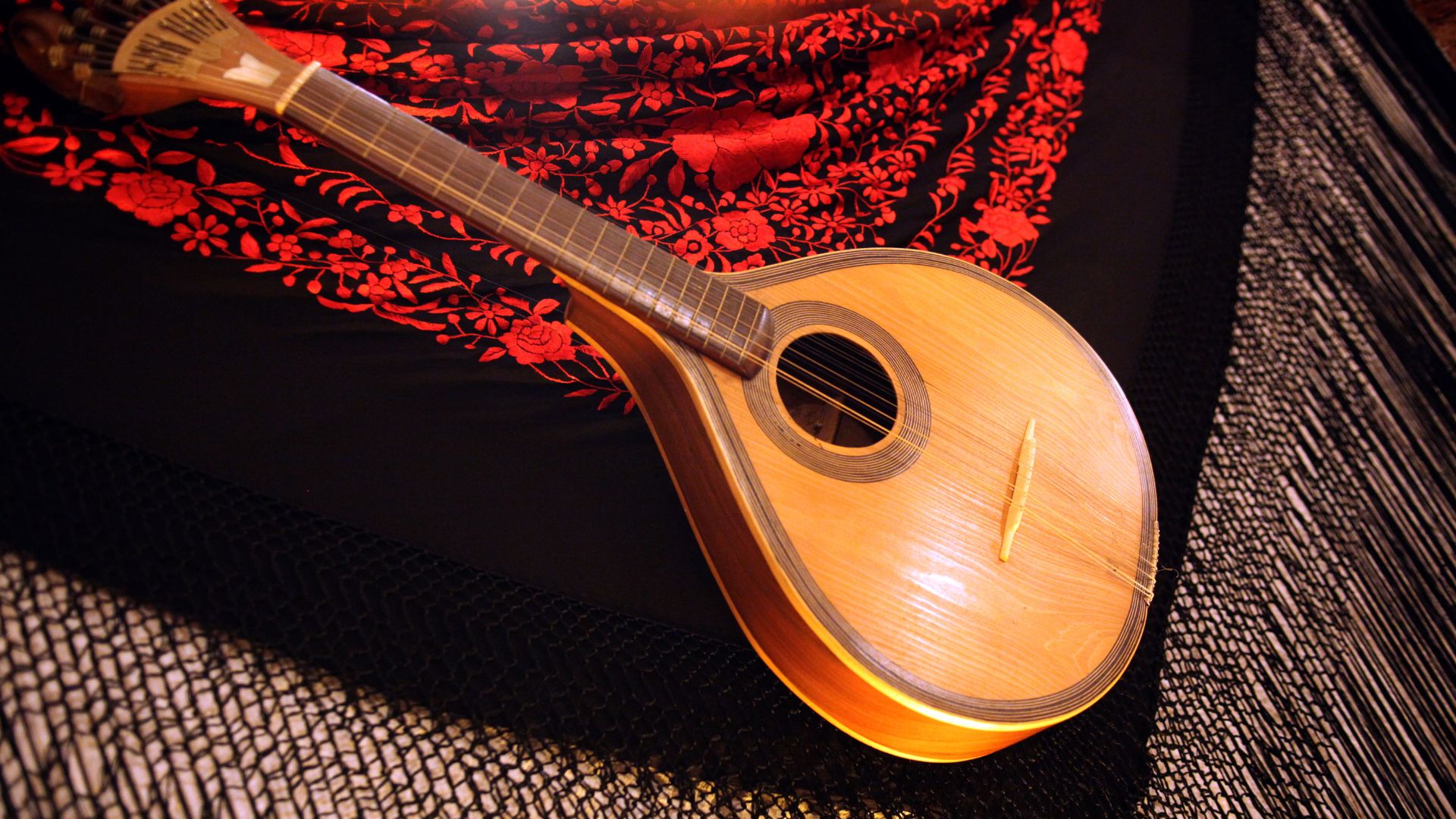 A Portuguese guitar with a teardrop-shaped body and a distinct headstock, resting on a dark fabric with red floral patterns.
