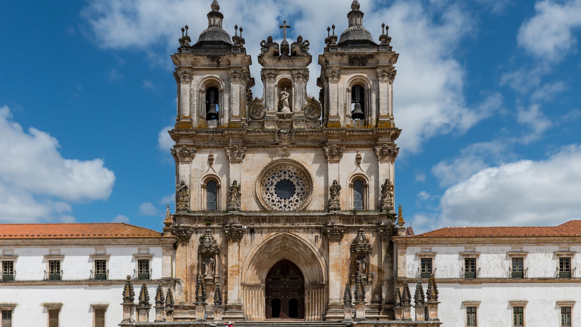 A grand, ornate stone monastery with multiple towers and spires under a partly cloudy sky.