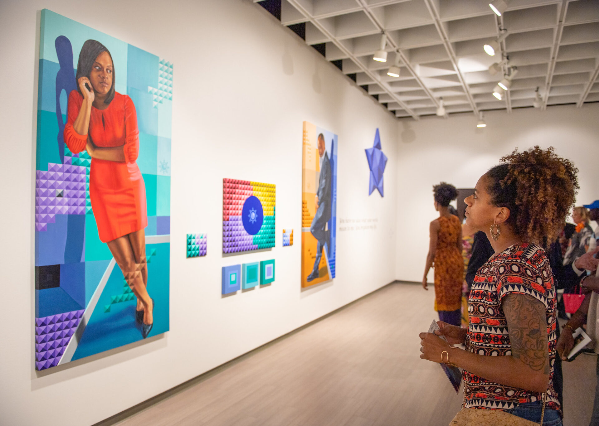 Several visitors casually walk and stand in a brightly lit, white‑walled teaching gallery—Anita S. Wooten Gallery at Valencia College, Orlando