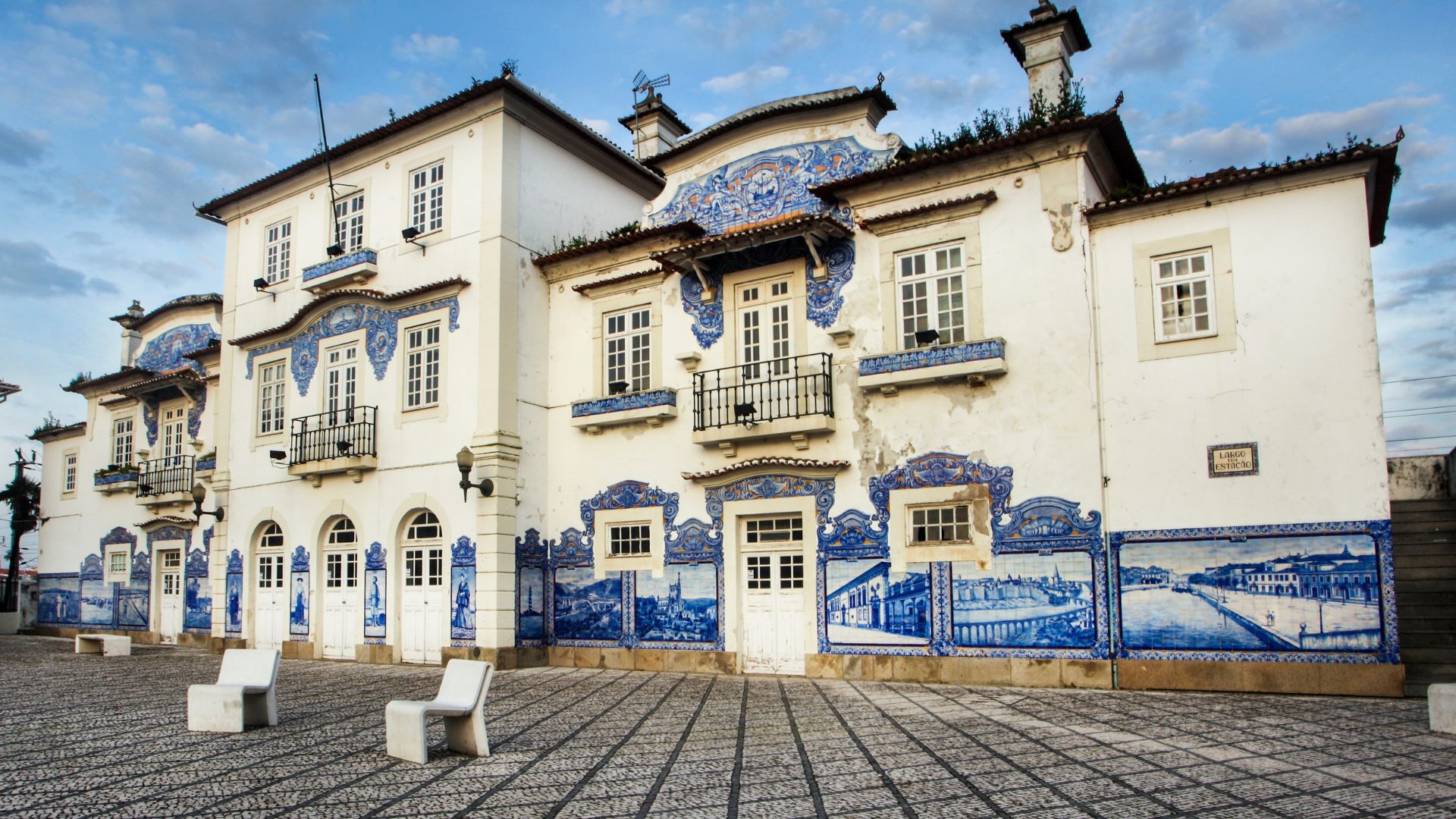 This image showcases the historic Aveiro Railway Station in Portugal, renowned for its facade adorned with monumental blue and white azulejo tiles depicting regional scenes, culture, and traditional activities.
