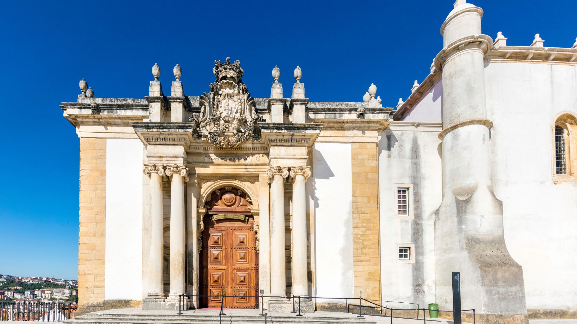A Baroque library building with a grand entrance and a tall, ornate tower against a clear blue sky.