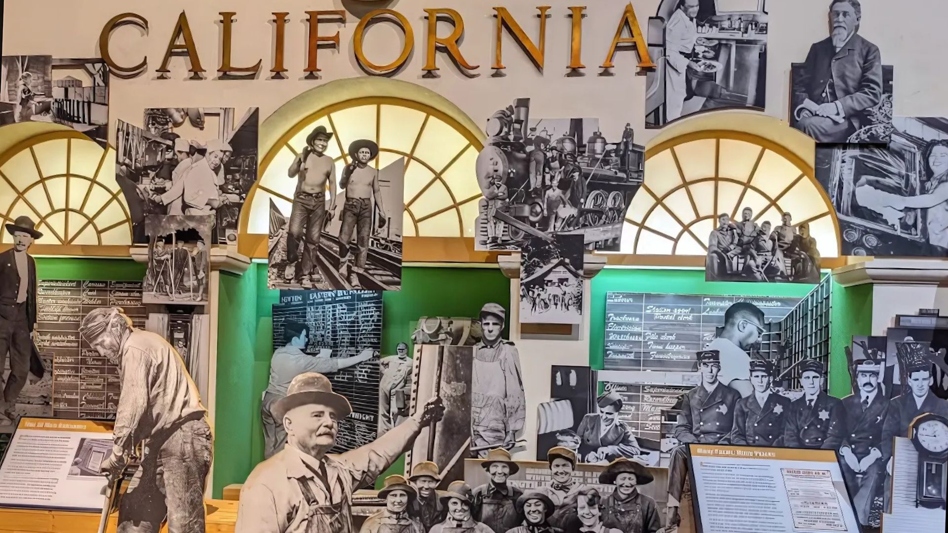 A large museum exhibit featuring the word "CALIFORNIA" prominently displayed above a collection of black and white historical photographs and cutouts depicting various aspects of early California life and railroad history, including workers, trains, and town scenes, set against a green and brown backdrop with arched windows.