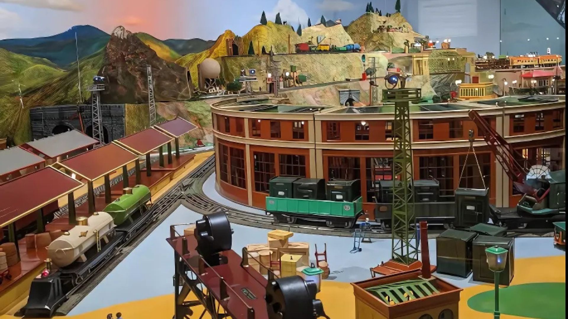 A detailed, sprawling model train exhibit featuring multiple tracks, trains, a roundhouse, station platforms, and miniature landscapes with hills and structures.